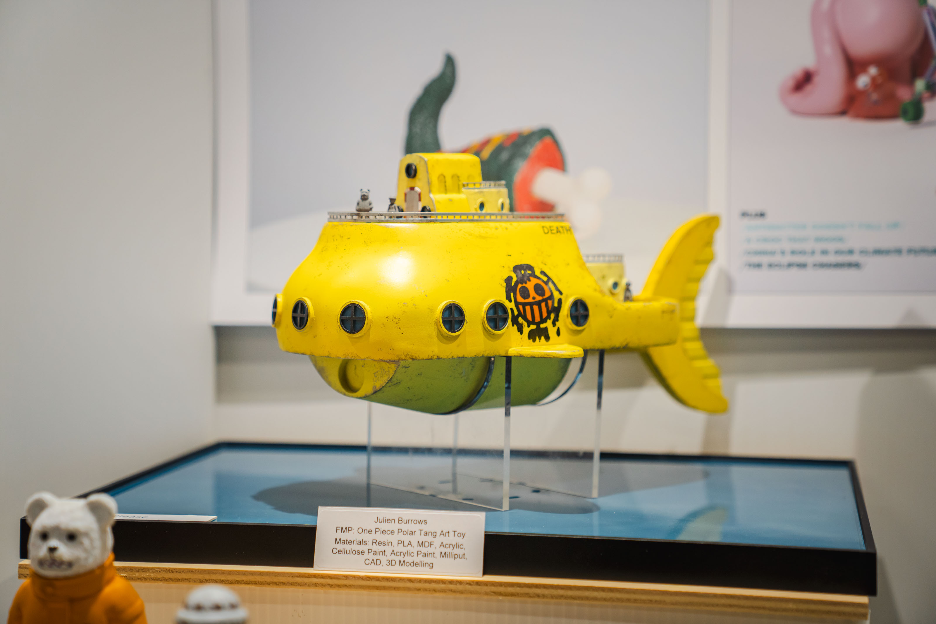 Yellow submarine model with green fin and red conning tower displayed in glass case at museum exhibition.