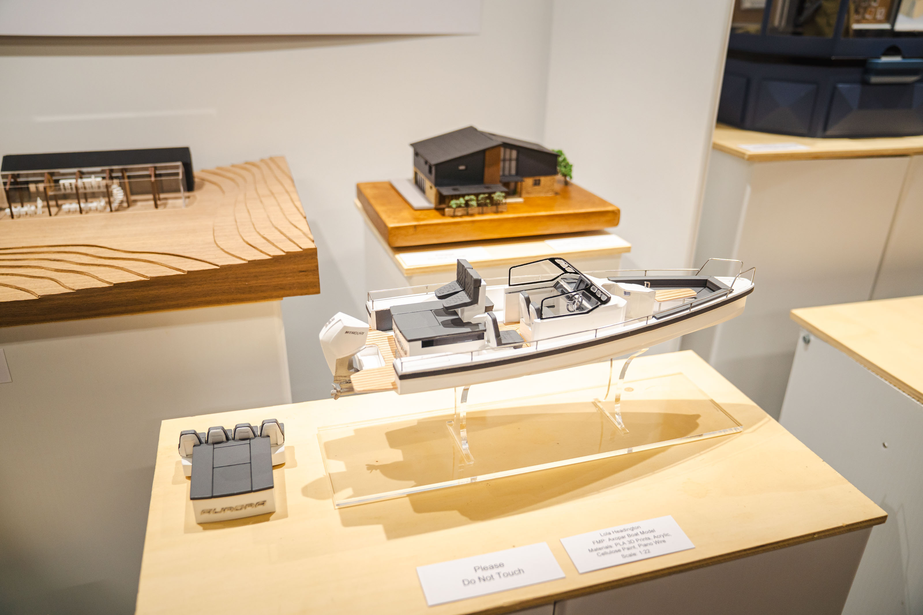 Display cases at New Blades Modelmaking expo containing architectural models and miniature structures on wooden platforms with white pedestals.