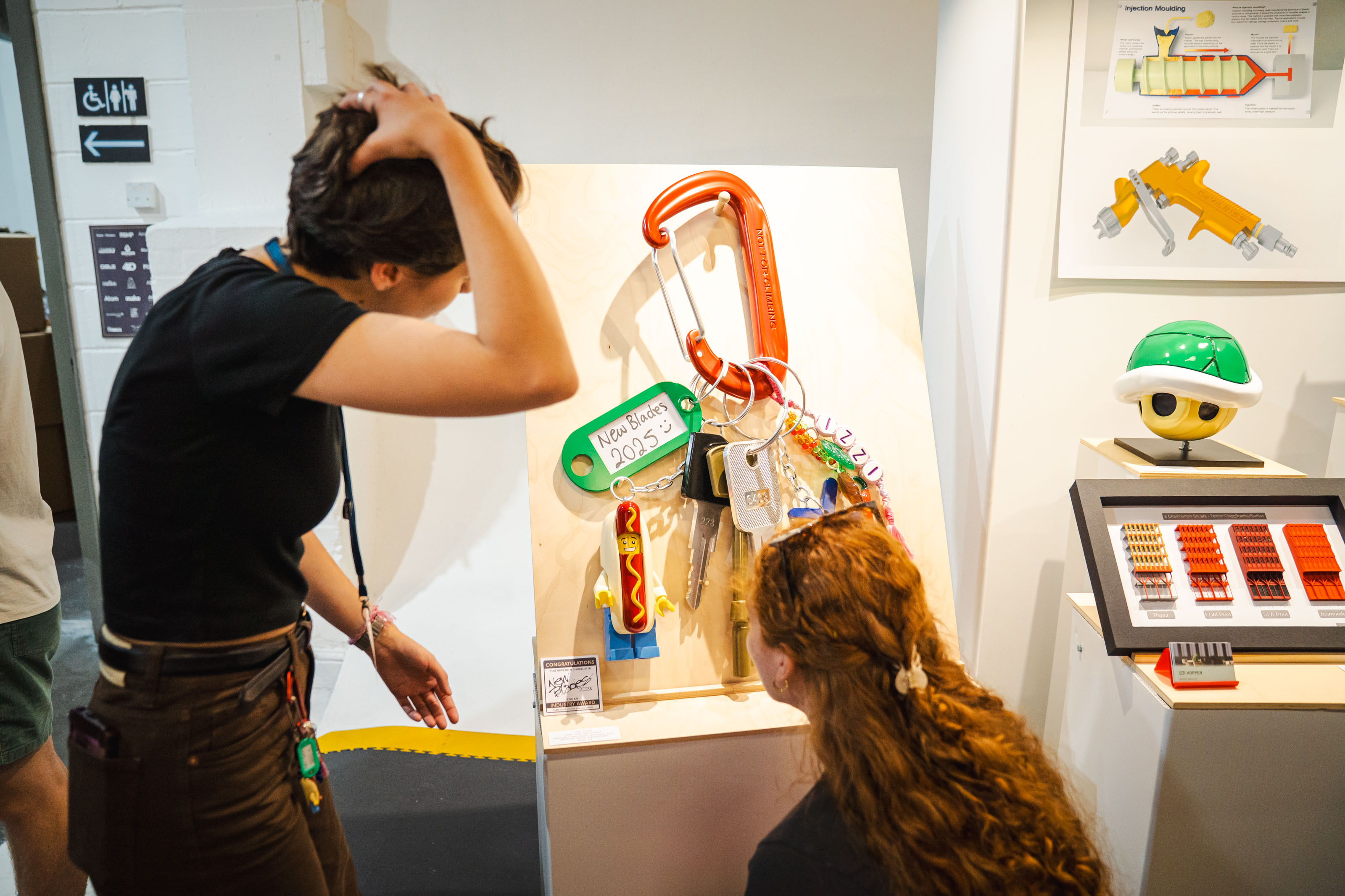 Two people with dark hair viewing a giant model key ring with keys and fobs, at New Designers, London.
