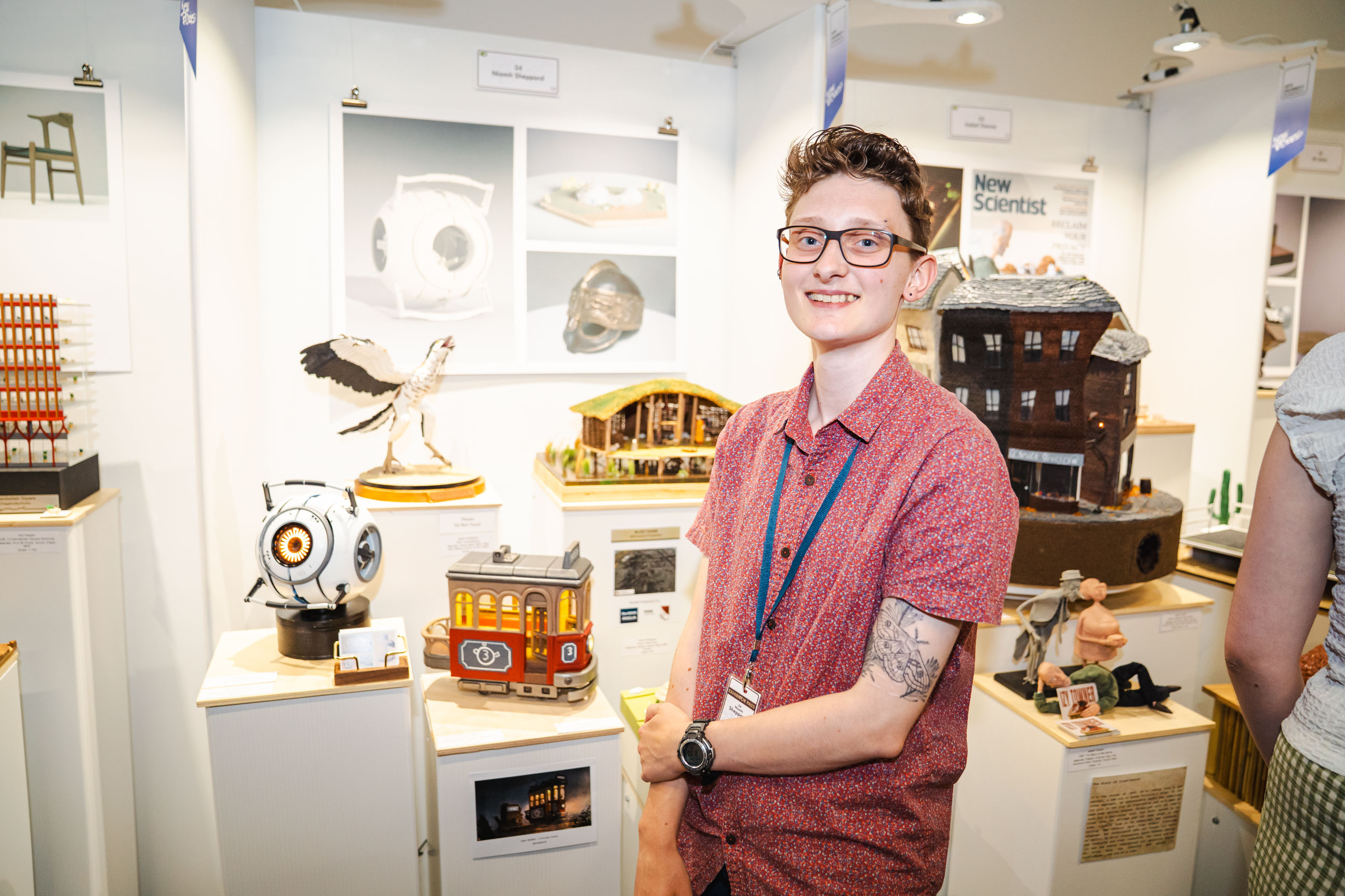 BA (Hons) Modelmaking graduate N Sheppard standing in front of assorted models on display on white pedestals.
