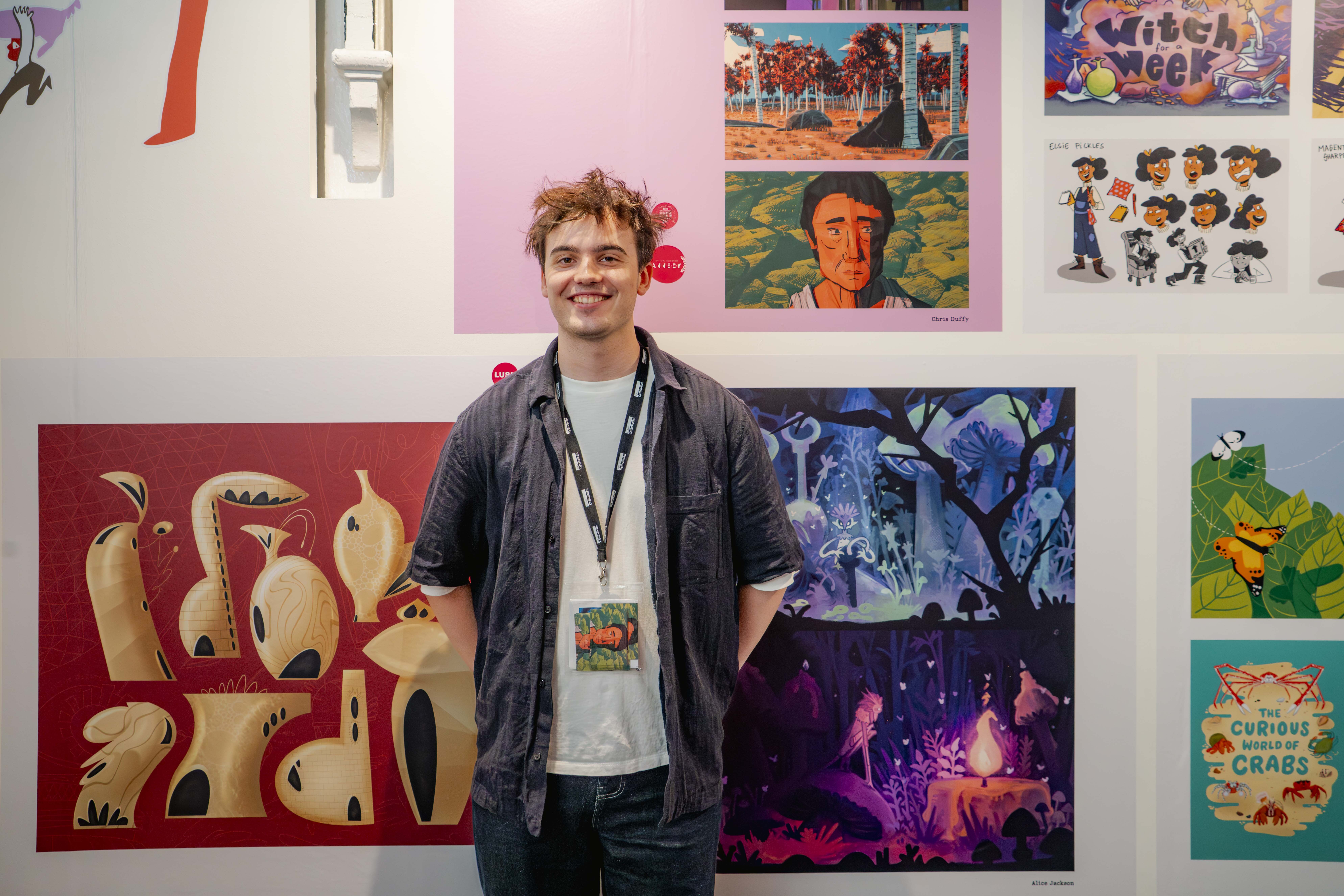 C Duffy stands before white wall displaying colourful artwork and illustrations.