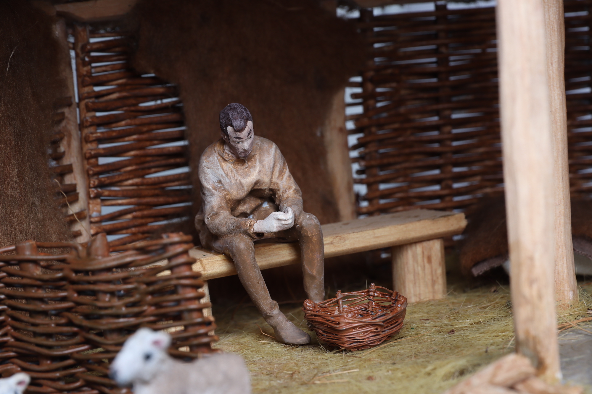 Close-up of a small-scale person in a traditional roundhouse, with lambs and wicker walls.