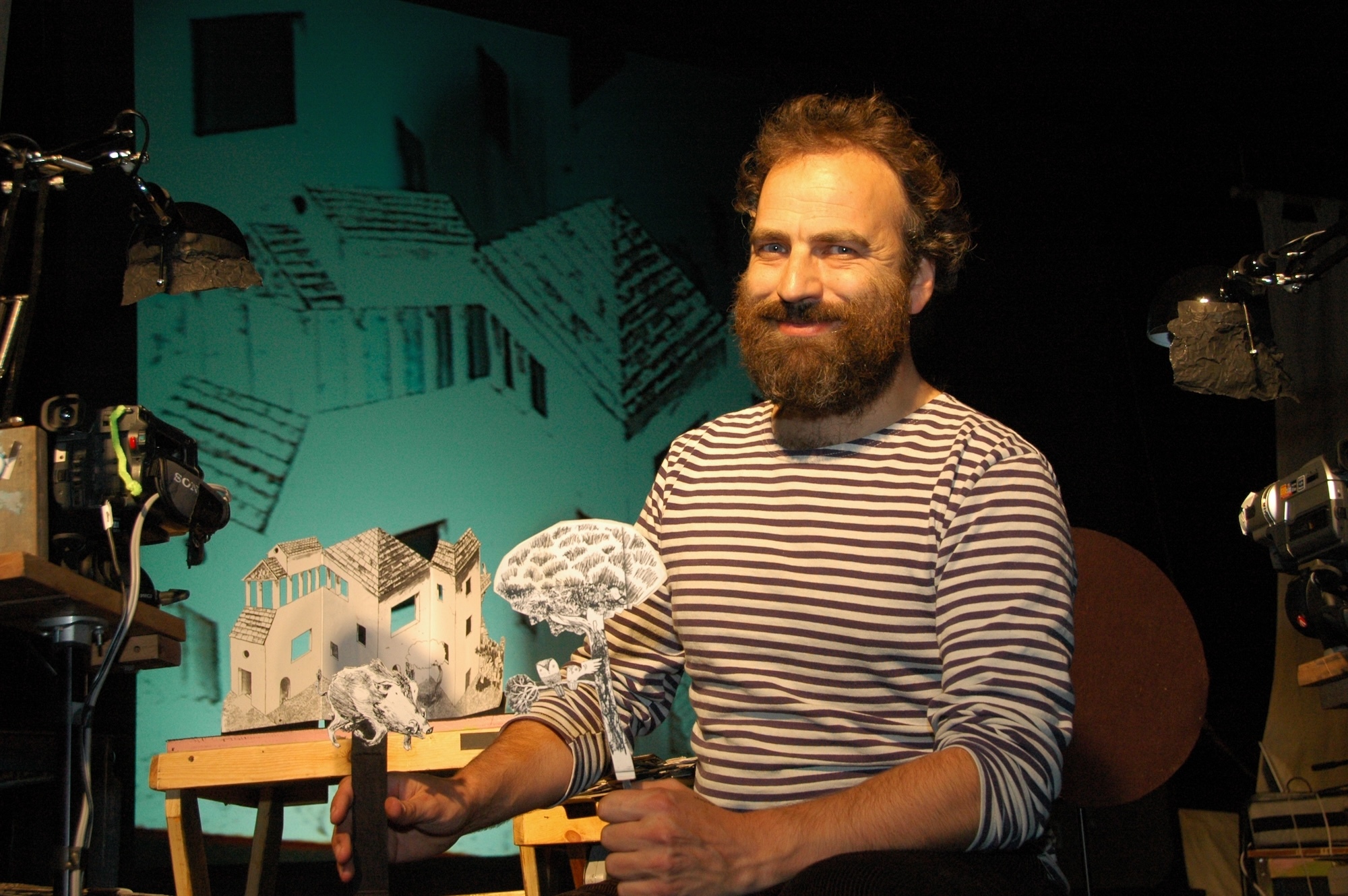 N Rawling smiling at the camera while holding paper puppets of a wild boar and a tree with an owl on a branch.