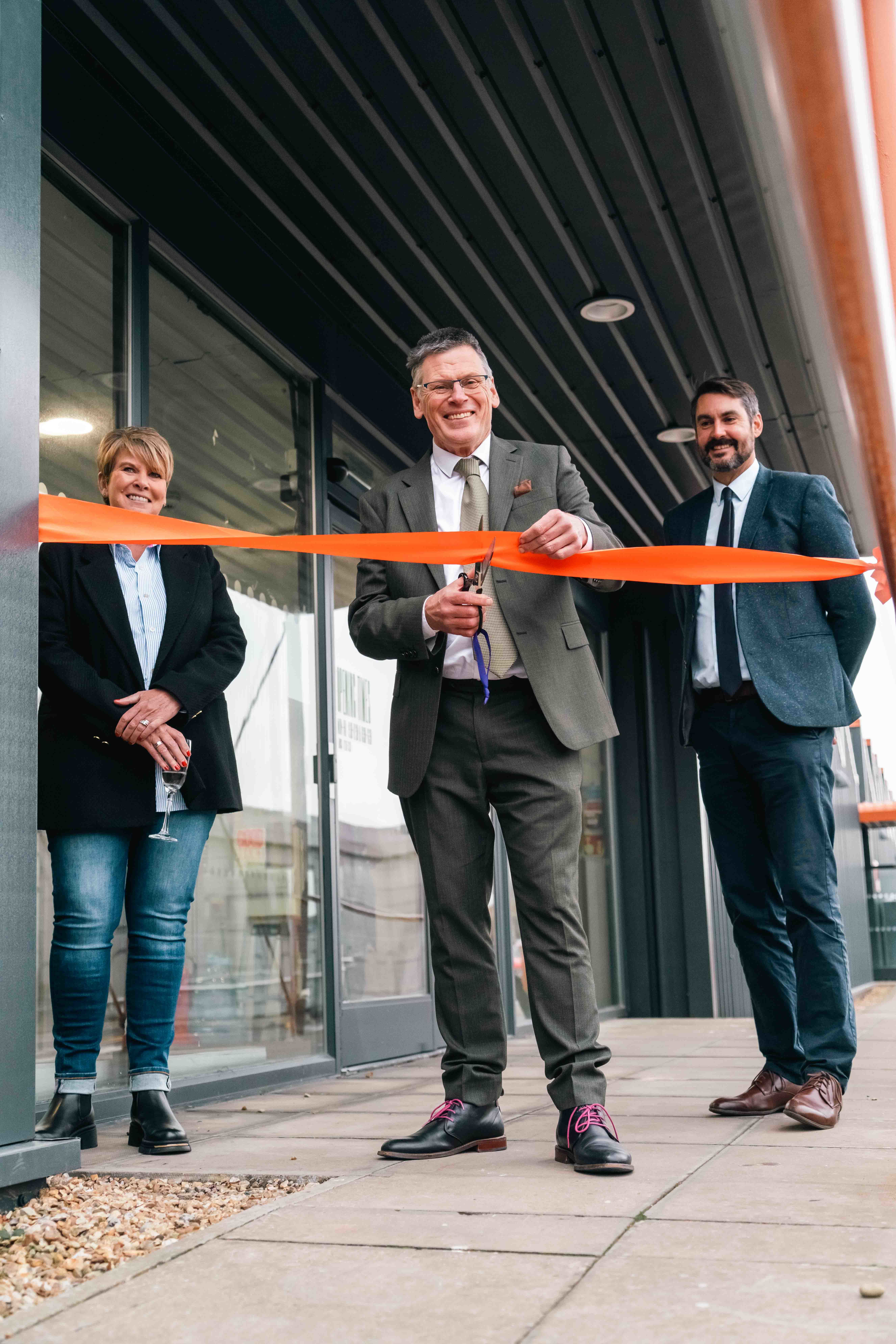 AUB Principal and Vice-Chancellor Professor P Gough preparing to cut a ribbon outside the North Lights Studios on AUB Campus. Two other members of AUB staff are standing behind him.