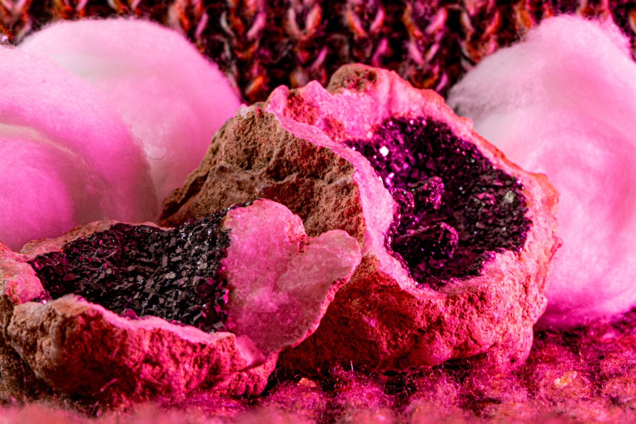 A pink and brown geode with glittering crystals and a small heart-shaped stone in the centre, surrounded by fluffy pink fibre in the background.