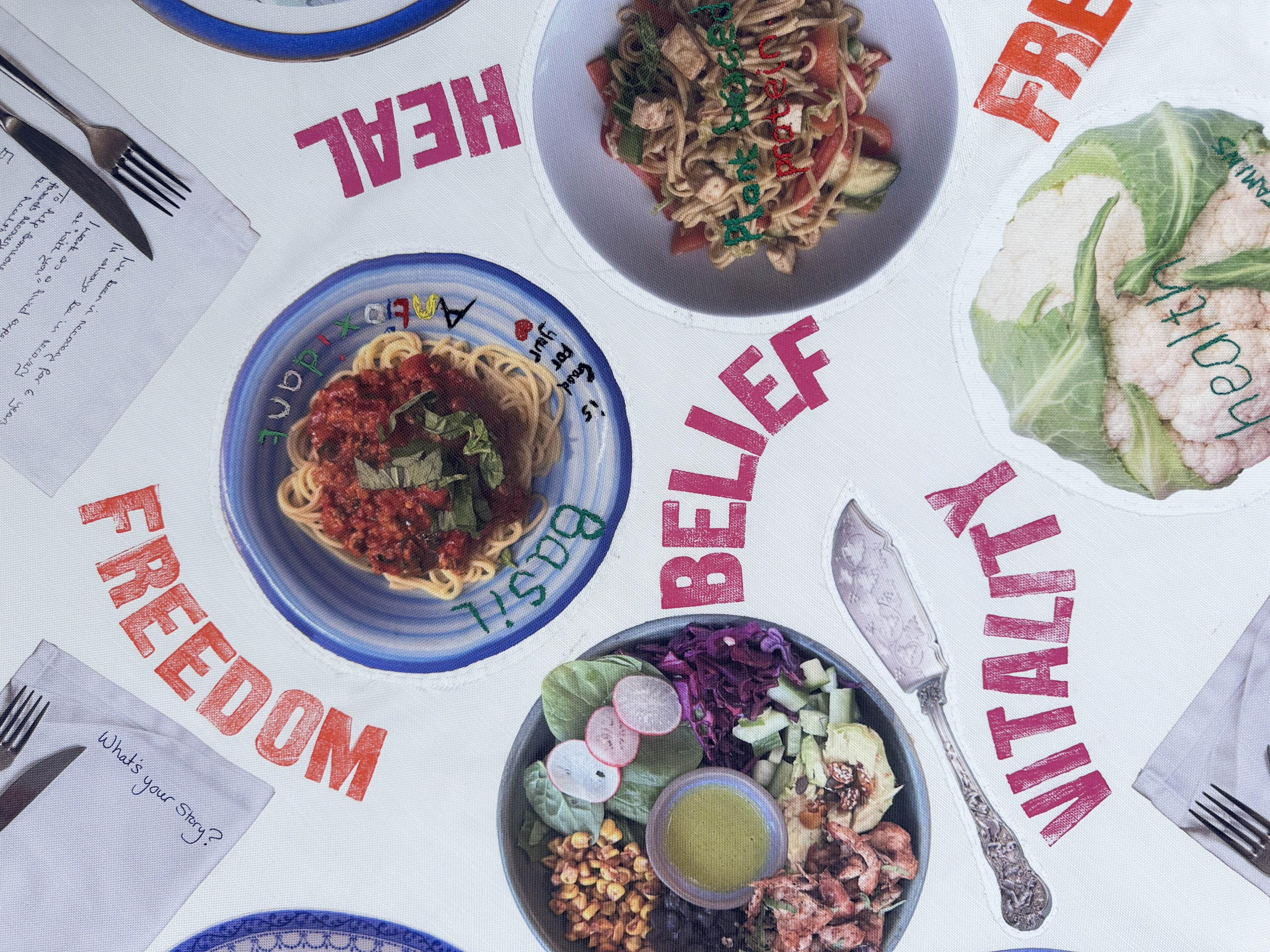 Three bowls of food on white table with red text reading "FREEDOM", "BELIEF", "HEALTH", and "VITALITY" scattered around plates and cutlery.