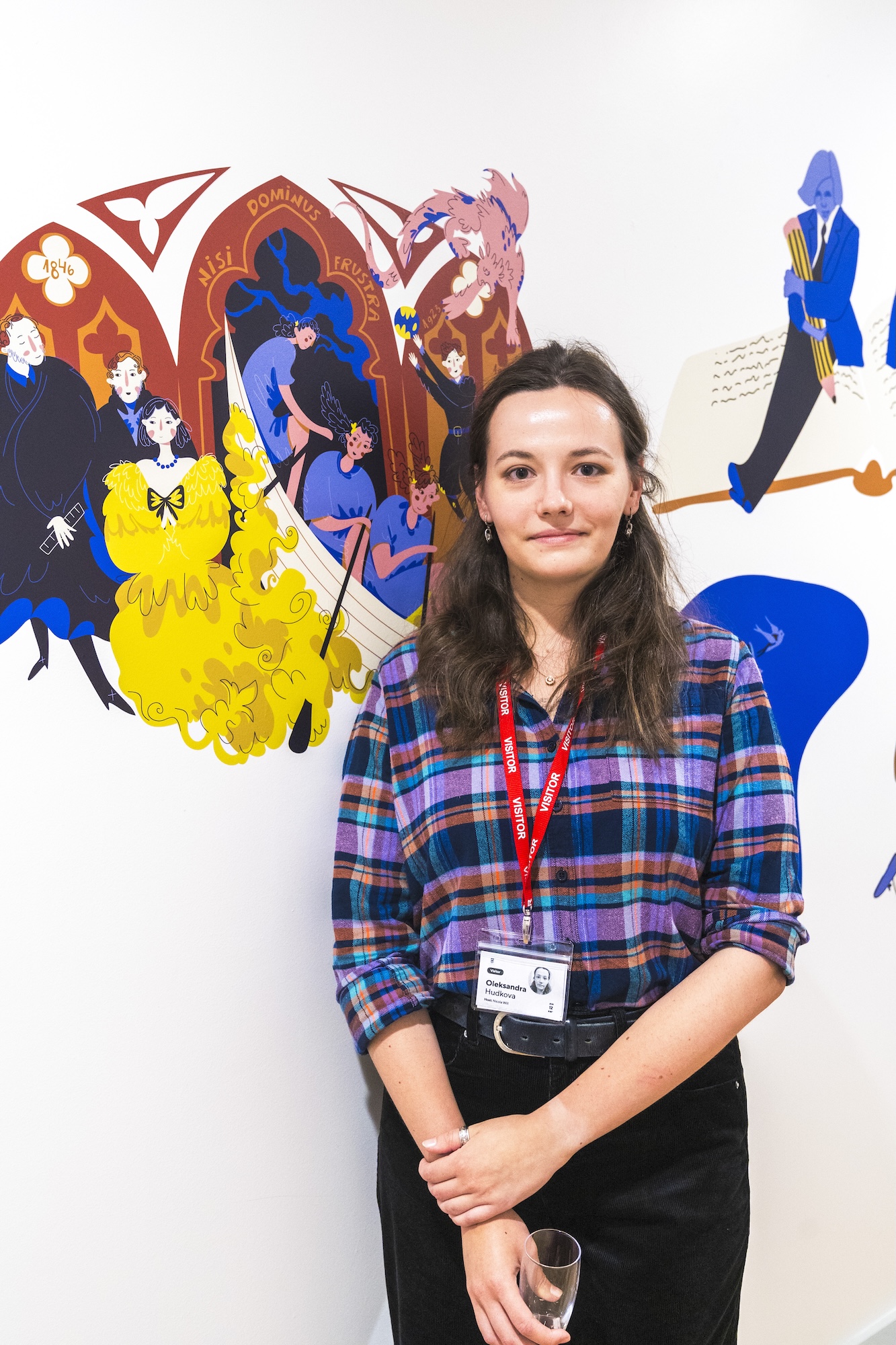 BA (Hons) Illustration student O. Hudkova posing for a photo in front of a vibrant wall vinyl illustration.