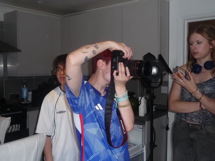 Three Arts University Bournemouth students standing in a Halls of Residence kitchen. One is holding a camera to their face.