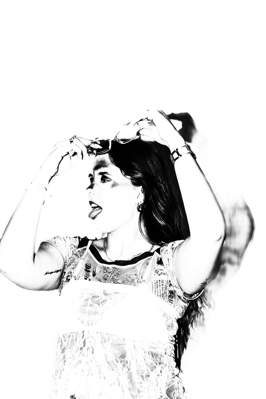 Black and white image of woman with dark bob haircut, hands raised to head, mouth open, wearing patterned top with light background.