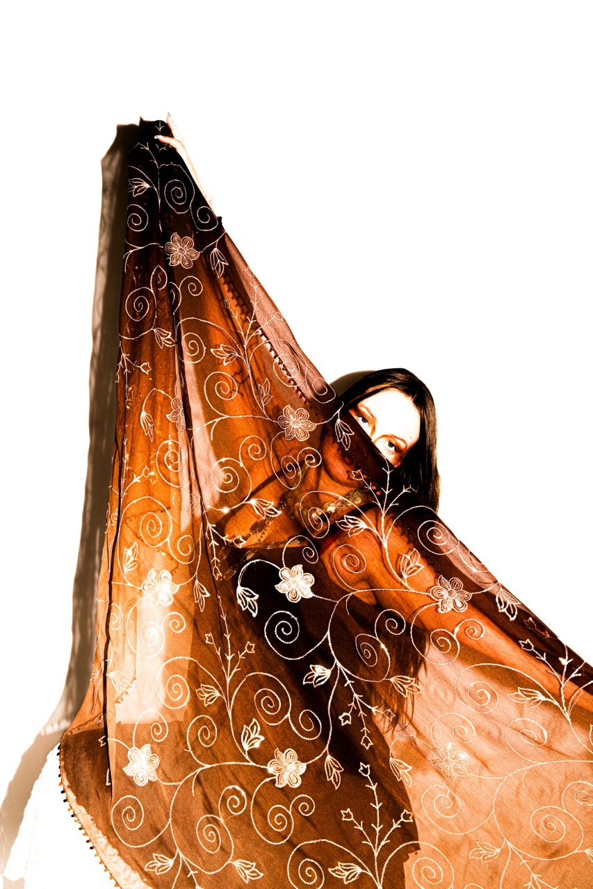 Orange and black embroidered shawl with floral swirl patterns held up by a model against white background, showing translucent fabric texture.