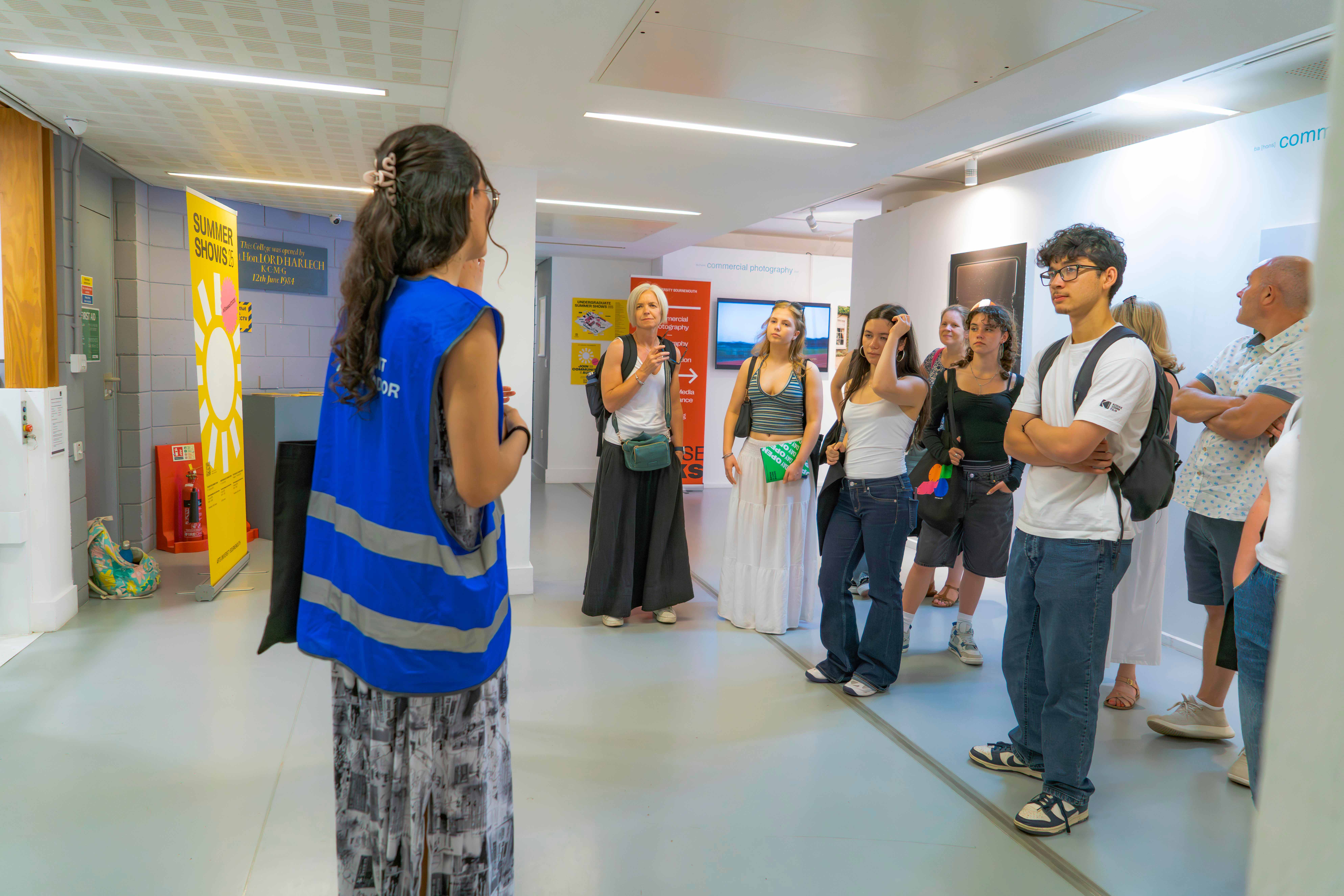 Student in blue high vis with back turned, talking to a group of people indoors.