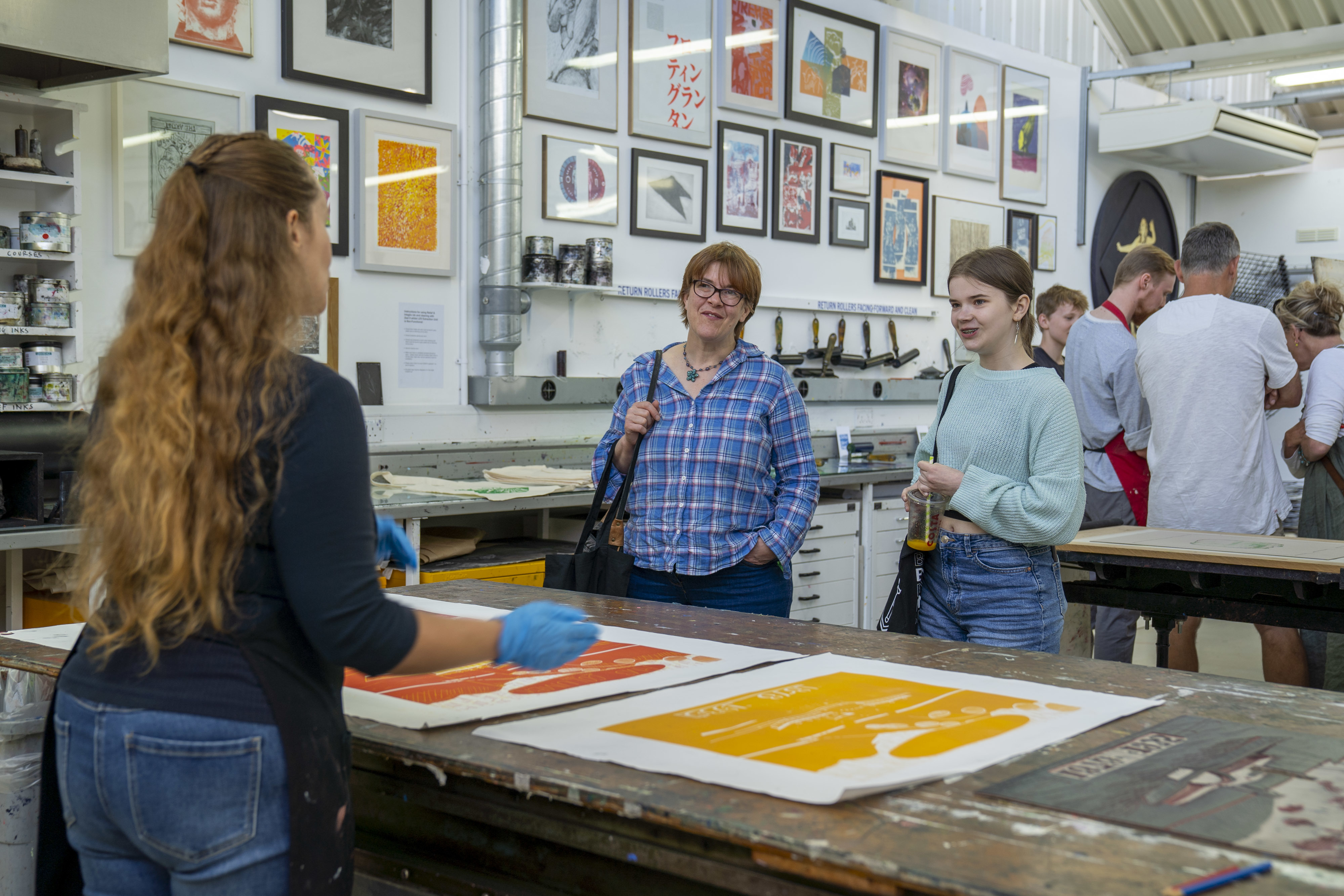 A young person and parent standing in the Print Room at Arts University Bournemouth while a staff member gives a printmaking demonstration.