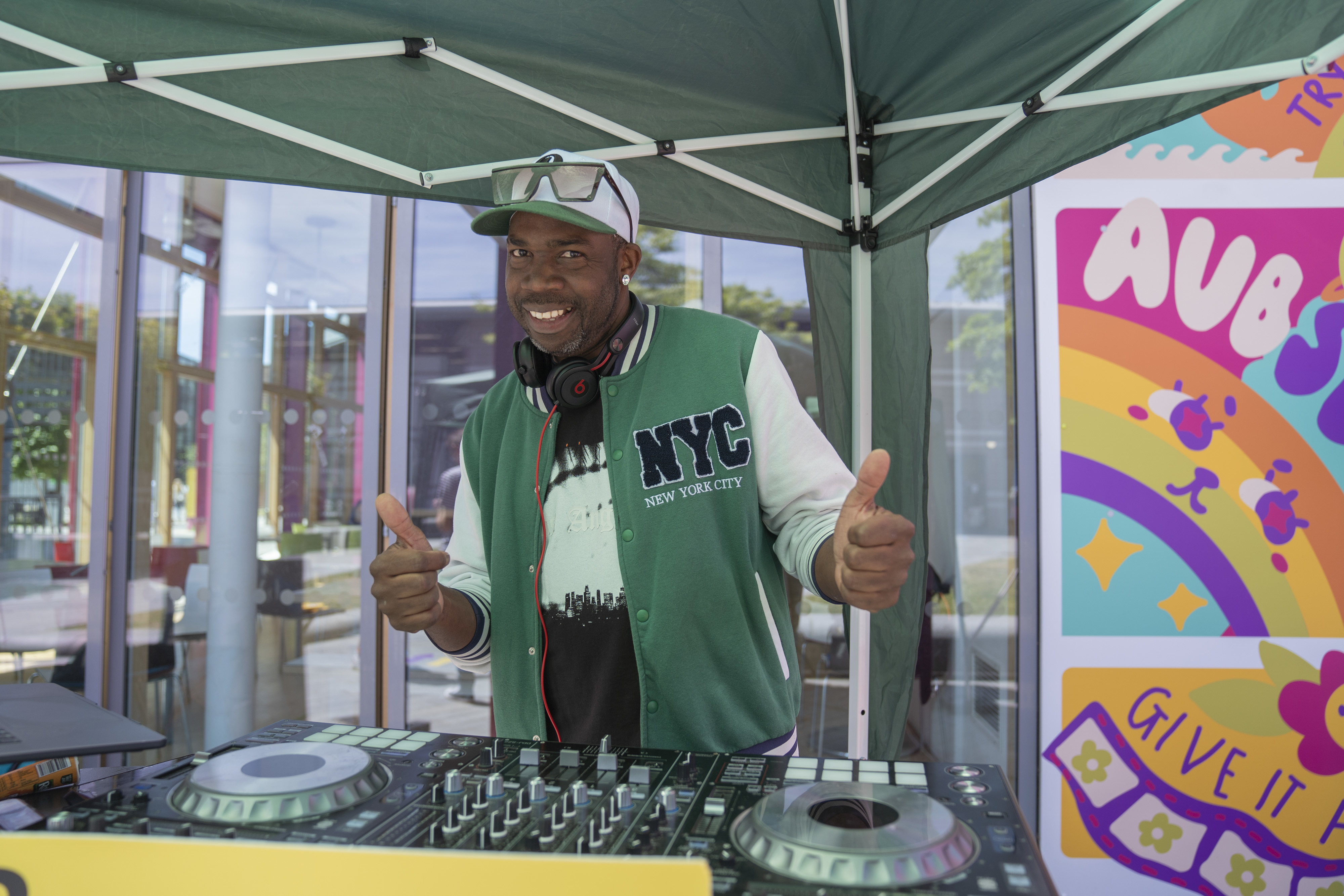 DJ Will at AUB's Open Day wearing a green NYC jacket under a green tent with a DJ set.