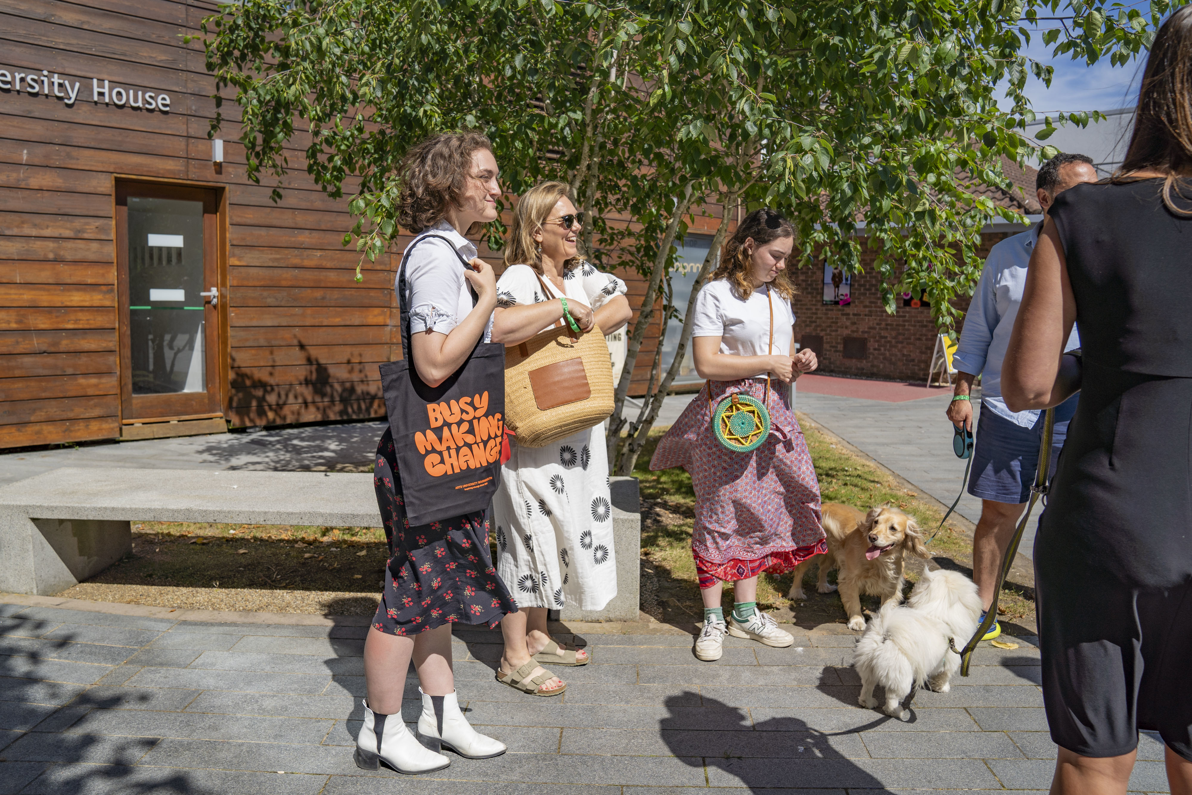 Three people and two dogs outside University House on AUB Campus at an Open Day.
