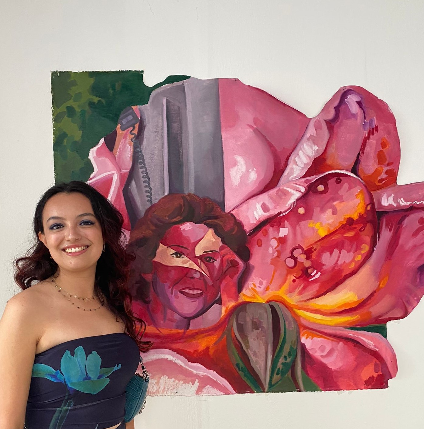 Liz Walker posed in front of her artwork blue and black floral top. The artwork is pink, abstract and has a face.