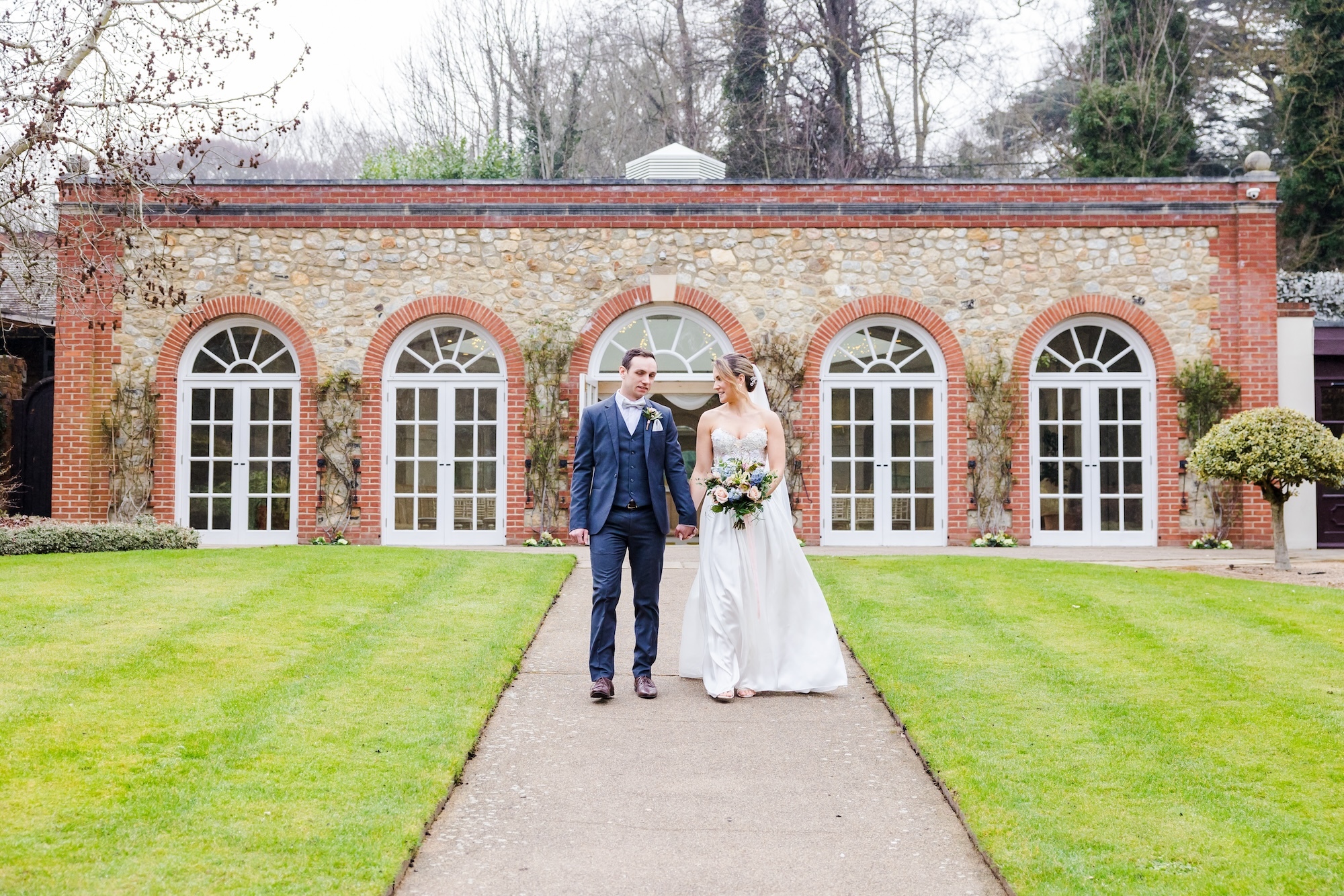 A bride and groom walking down a path from a stately building.