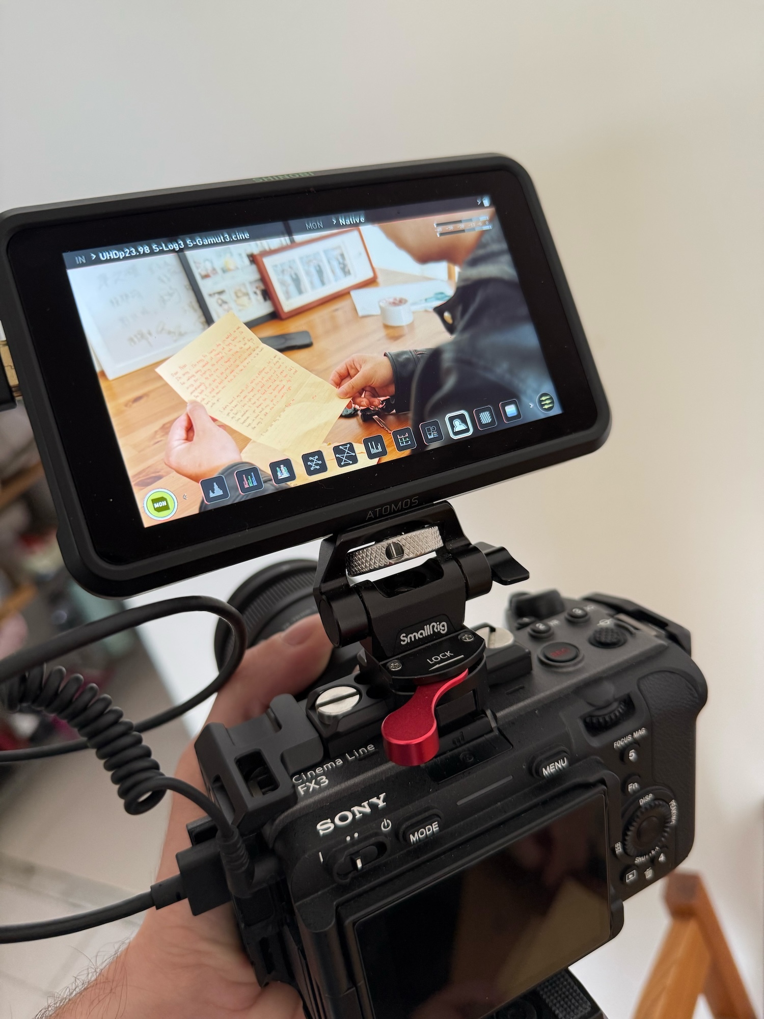 Close-up of a camera with a Small Rig monitor attached. The monitor shows a person sat at a table reading a letter.