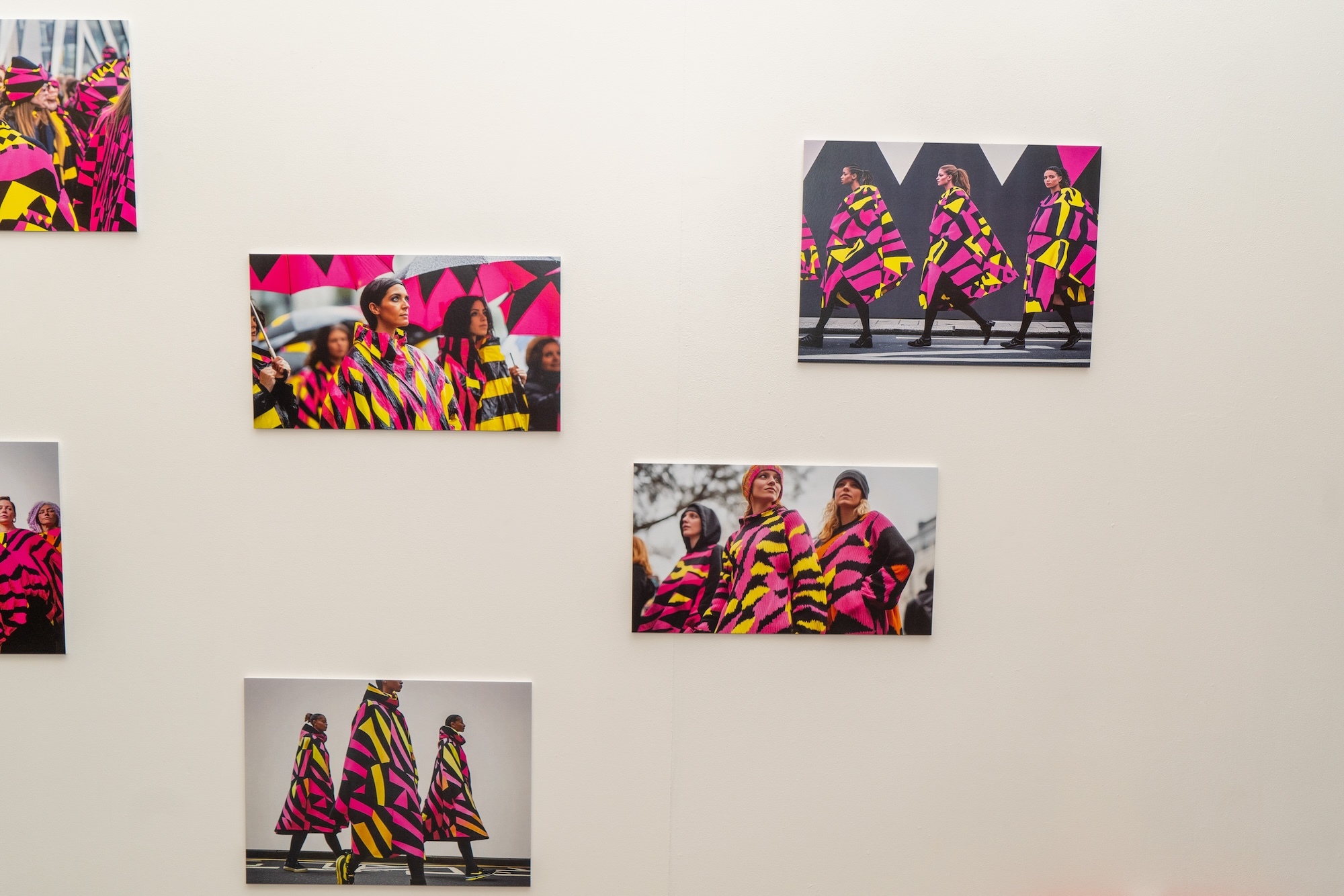 Several small photo-style images showing digital models wearing various yellow, pink and black outfits, on display on a gallery wall at Arts University Bournemouth.