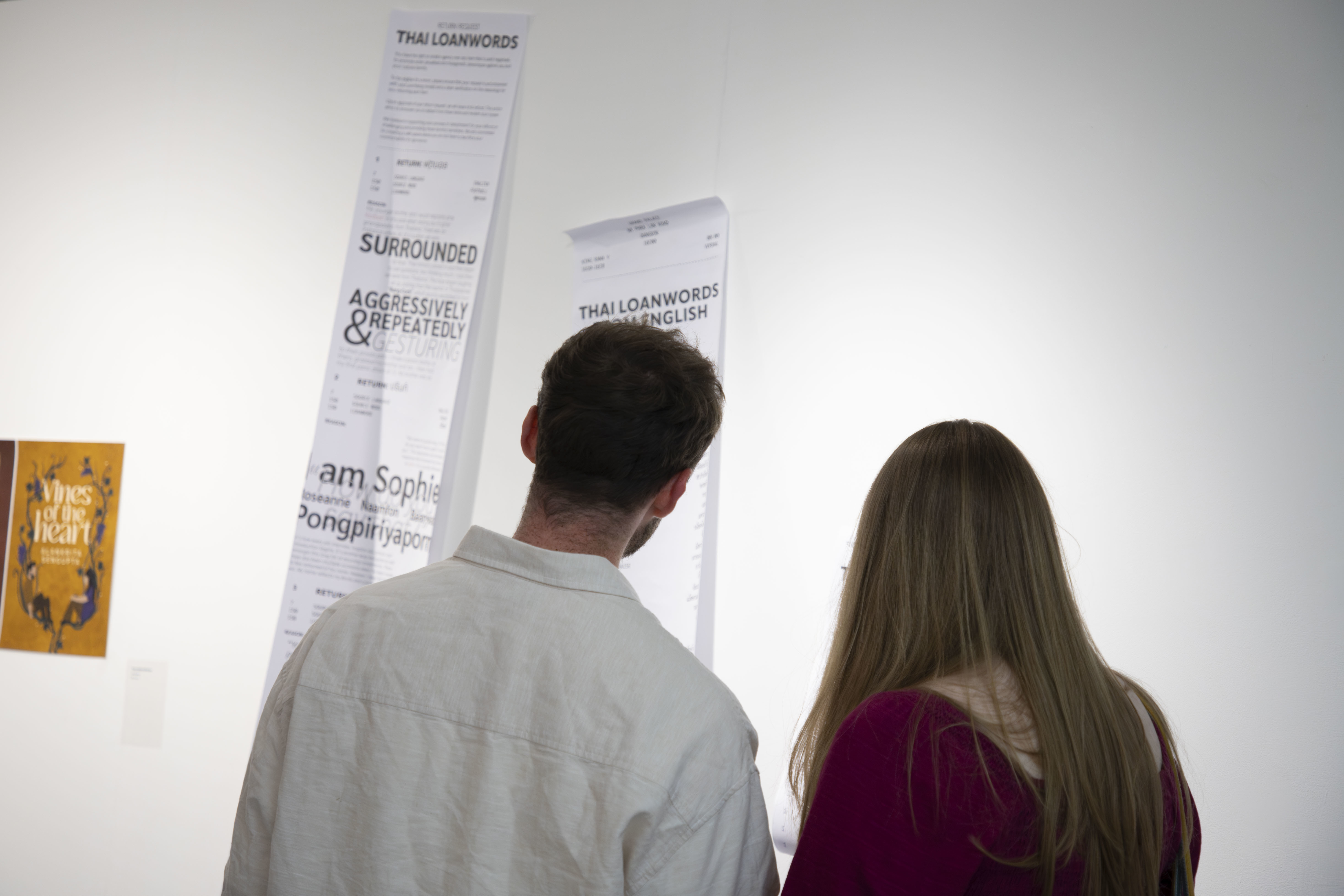 Two people viewed from the back looking at artworks displayed at TheGallery, AUB Campus, during the 2024 Postgraduate Summer Shows.