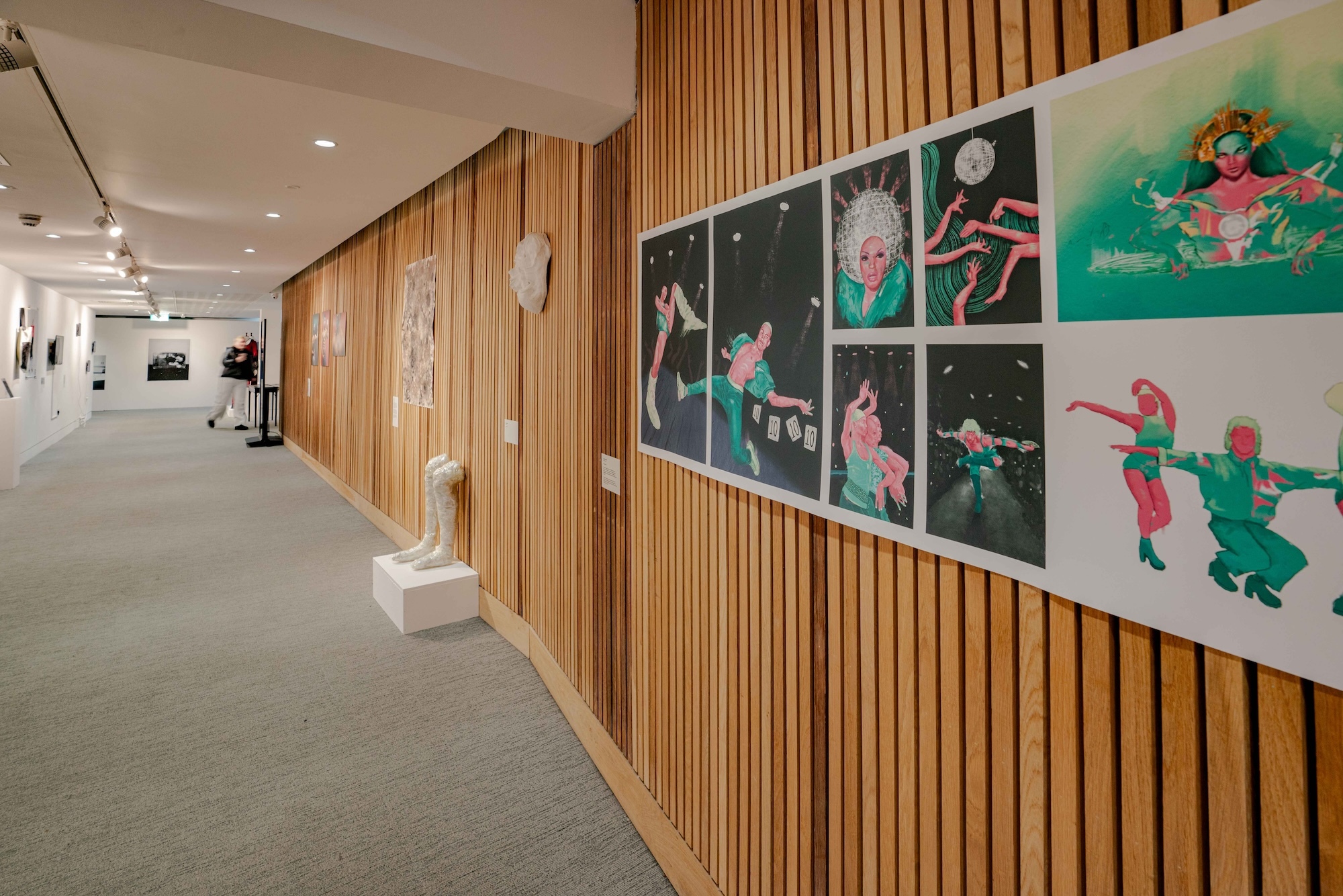 A series of illustrations showing people in various vogue poses on display on a wall at TheGallery, Arts University Bournemouth. Other exhibits are visible further down a long gallery corridor.