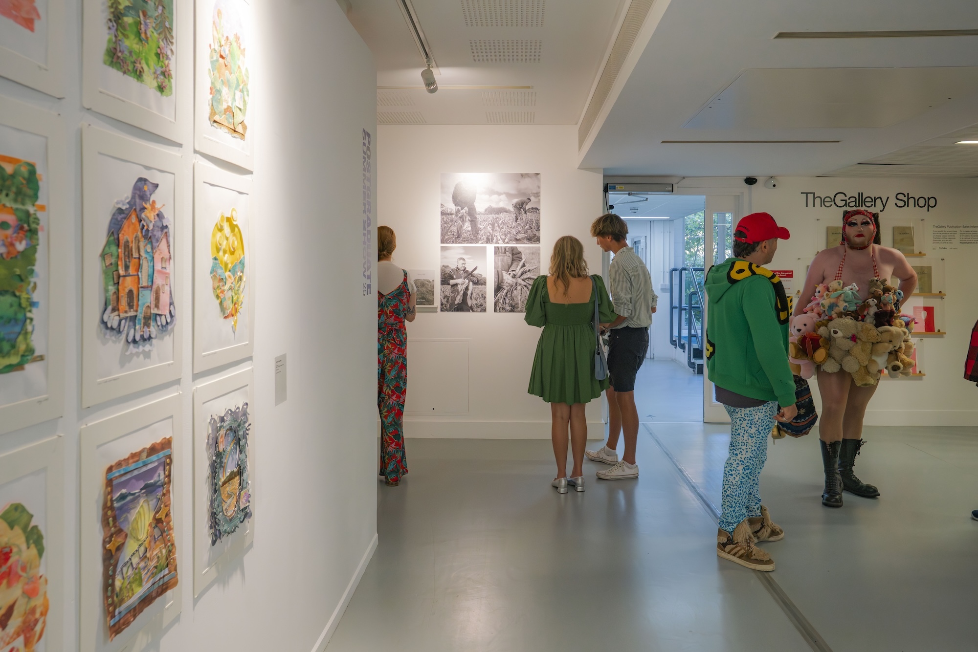 White gallery interior with colourful framed artwork on left wall, visitors viewing black and white photographs, shop entrance visible.