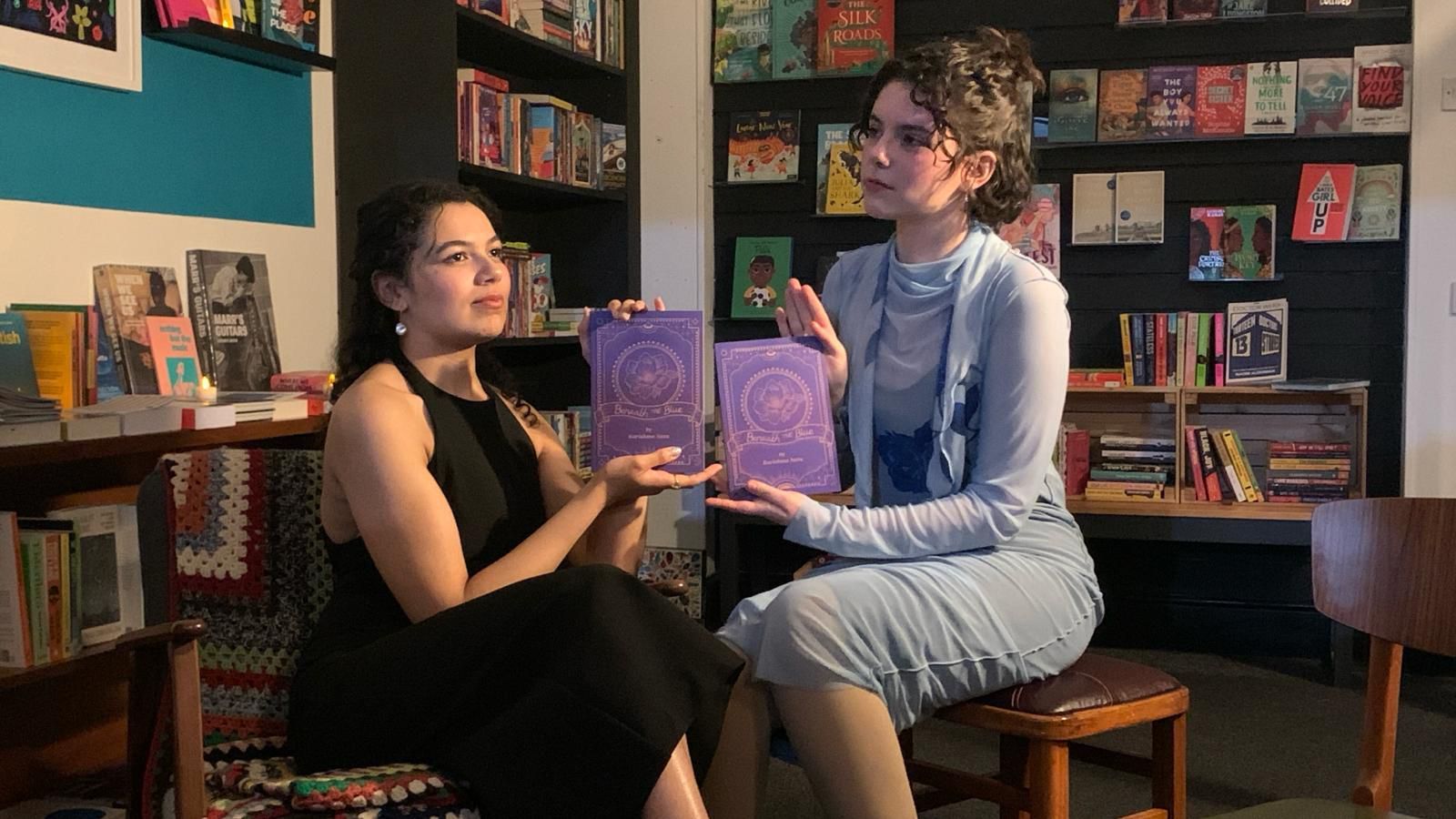 Karishma Natu and Victoria Grant sat posing for the camera in Bookbag, holding copies of 'Beneath The Blue'.