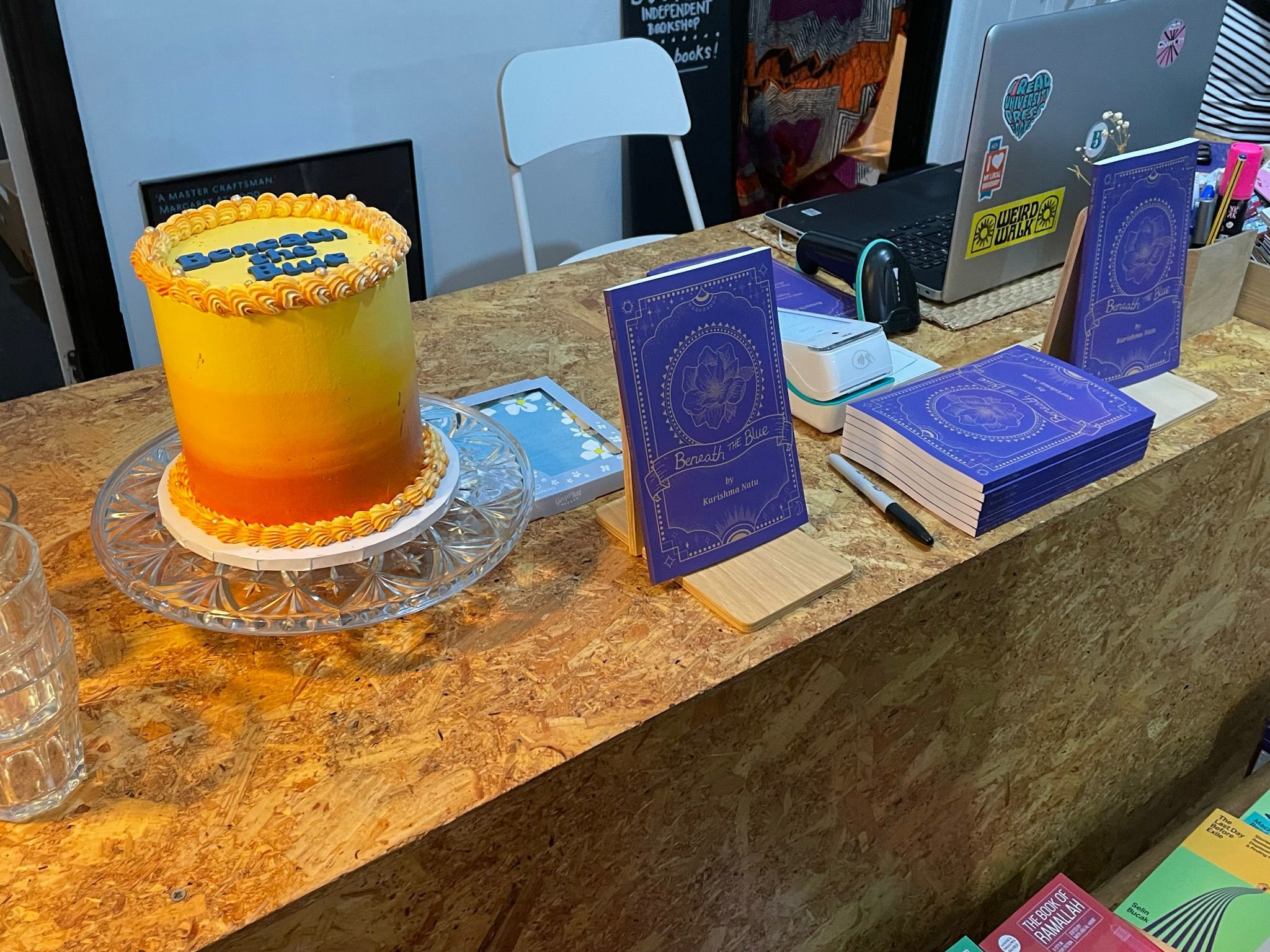 A table at Bookbag with Karishma's book and a tall, sunset-gradient cake.