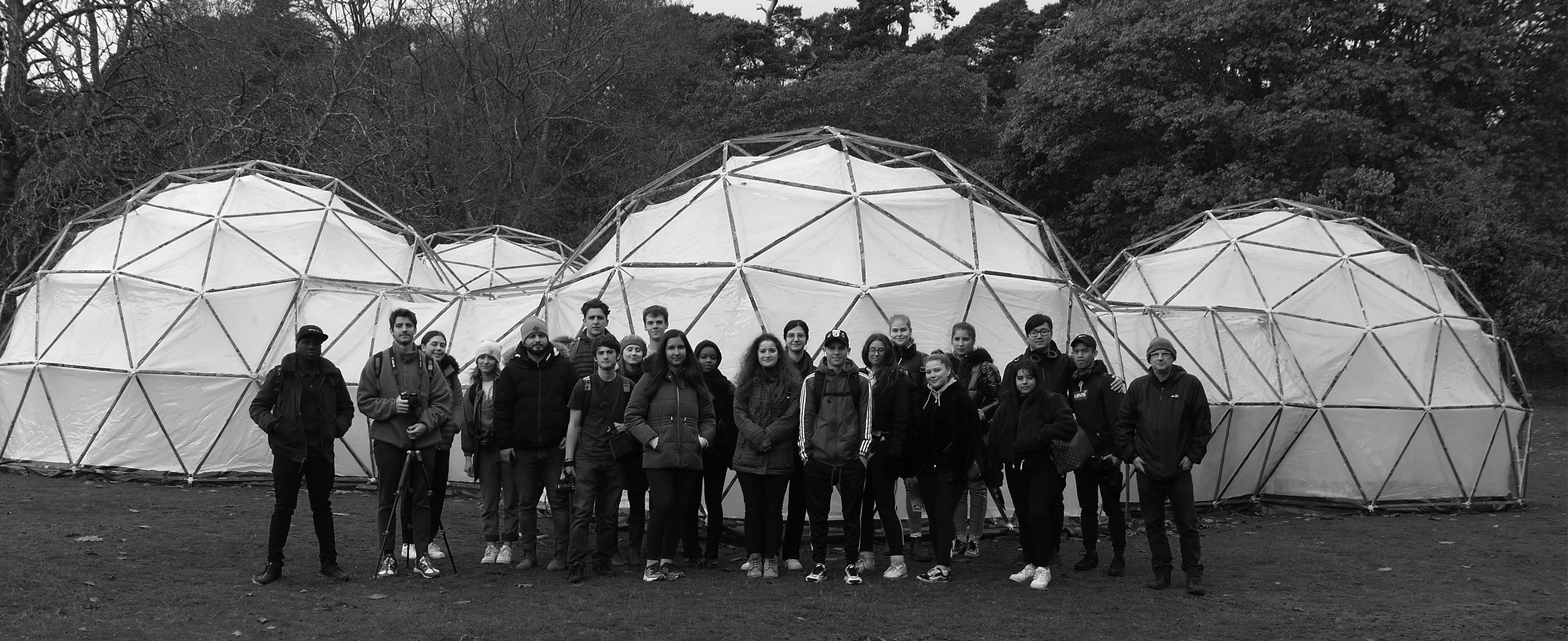 A crowd of people gathers and poses for a photo in front of a series of domed structures in a field.