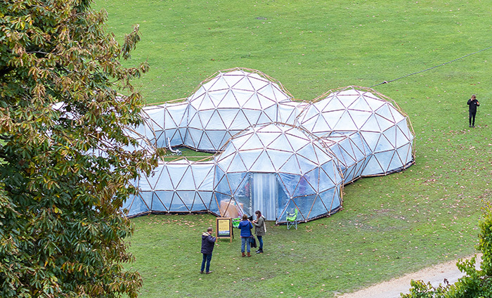 A series of domes set up in a field with a few people standing outside them.