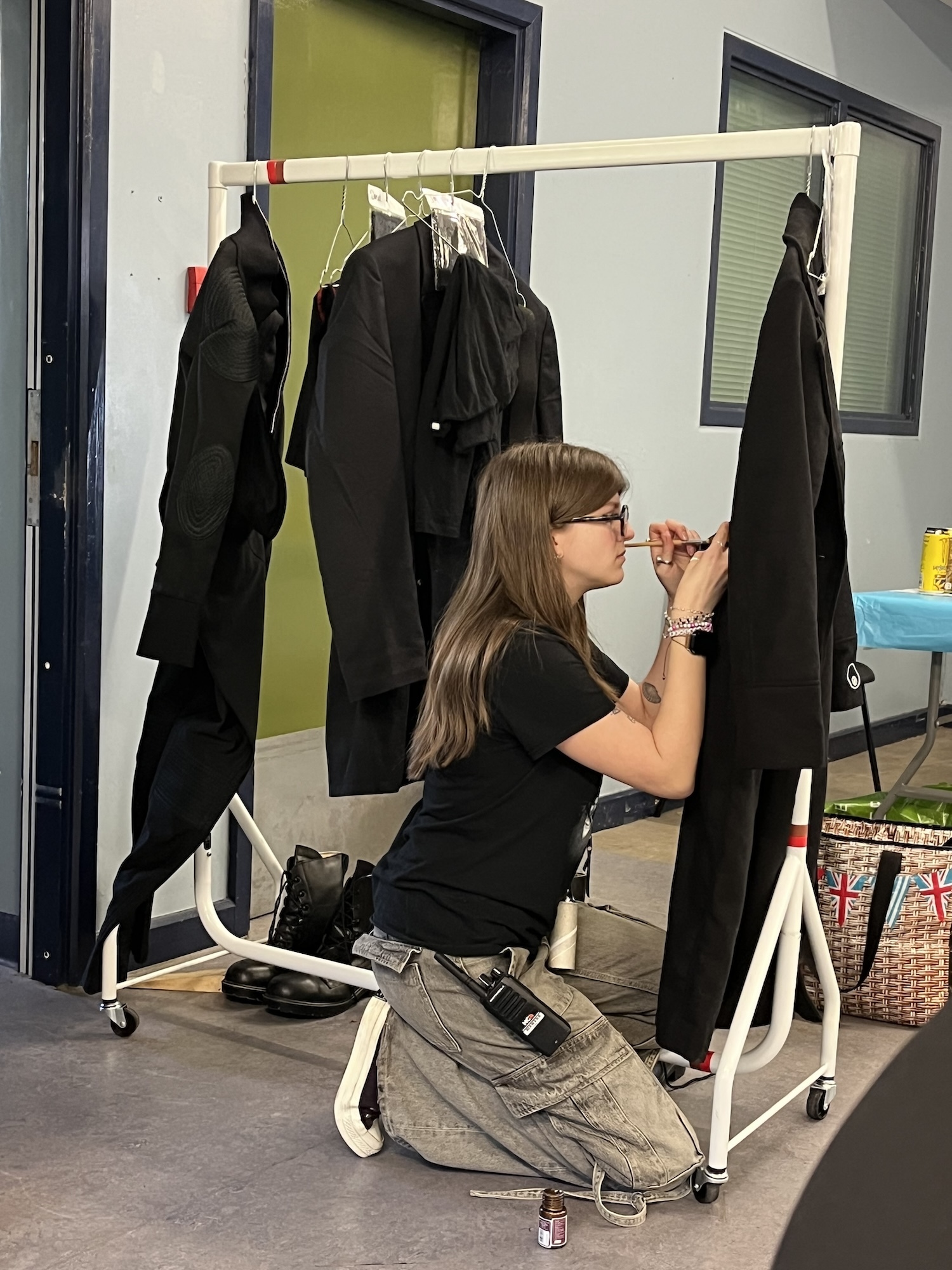 A BA (Hons) Design for Costume and Performance student kneels down by a clothes rail and makes adjustments to the back of a long, black coat.