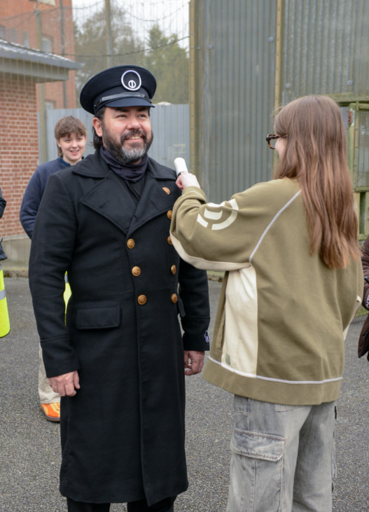 A BA (Hons) Design for Costume and Performance student makes an adjustment to a long military jacket being worn by an actor, on the set of "Paper Tiger".