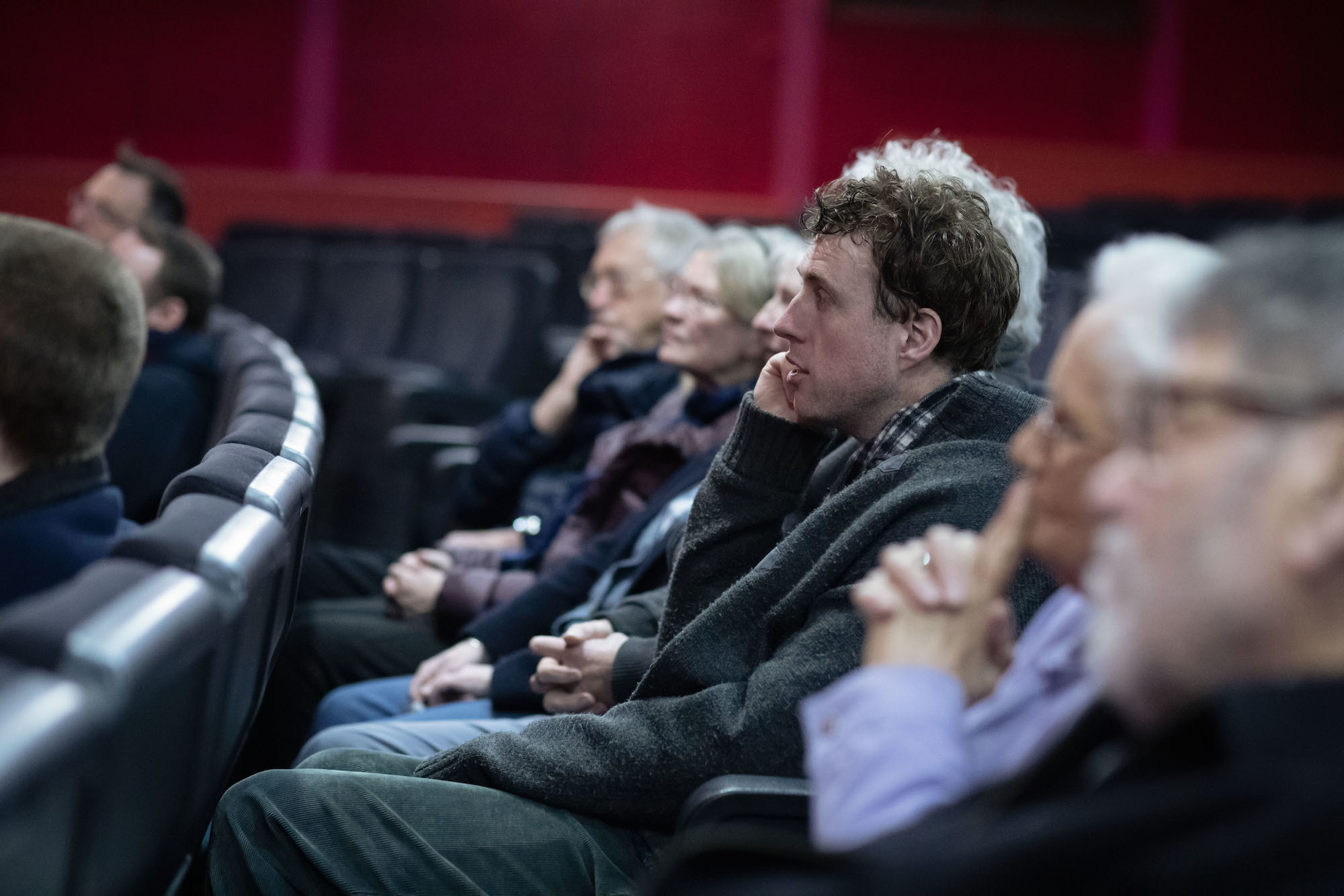 Members of a theatre audience sitting in a row of seats.