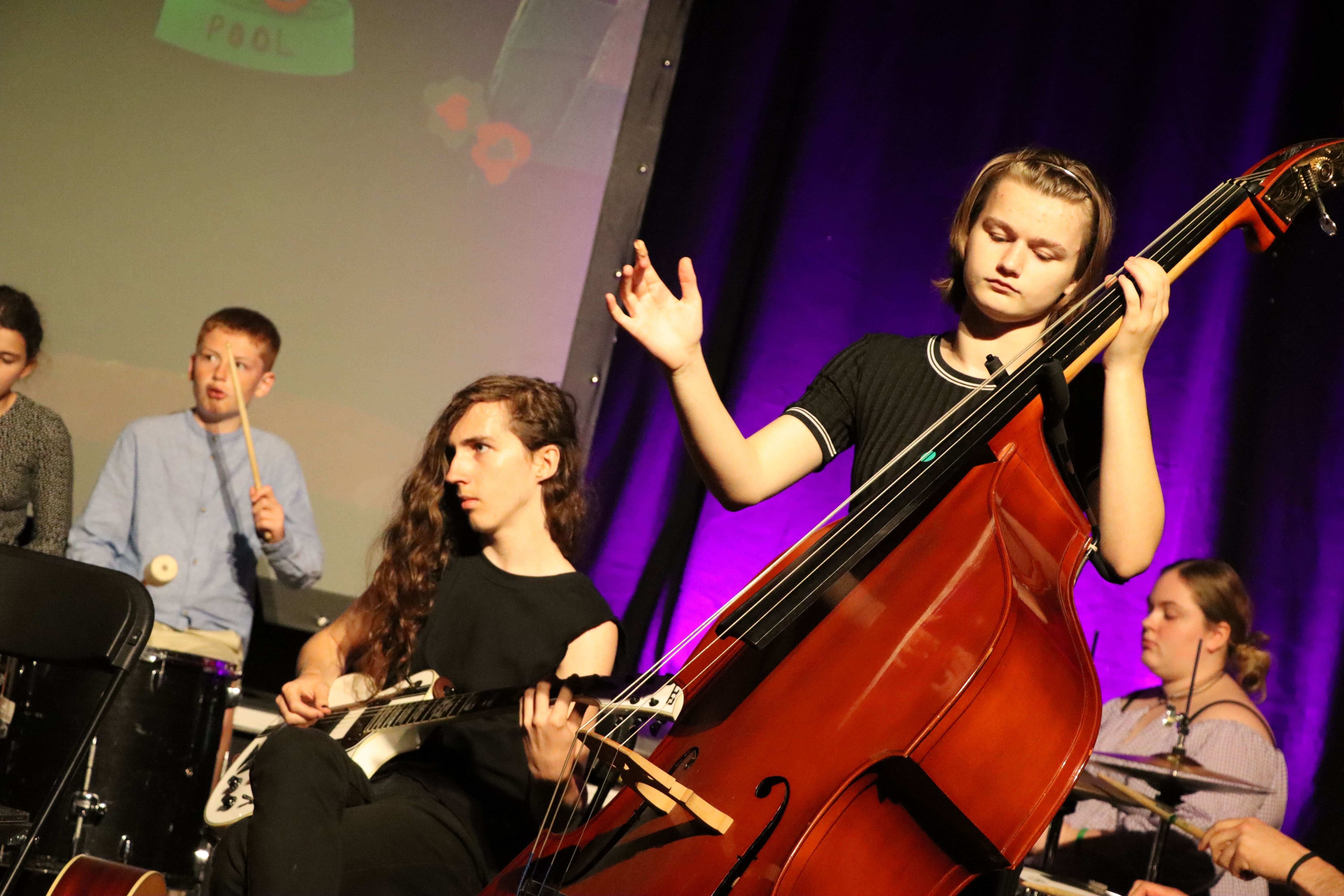 Young people playing musical instruments including drums, guitar and double bass on stage at the Palace Court Theatre, Bournemouth.