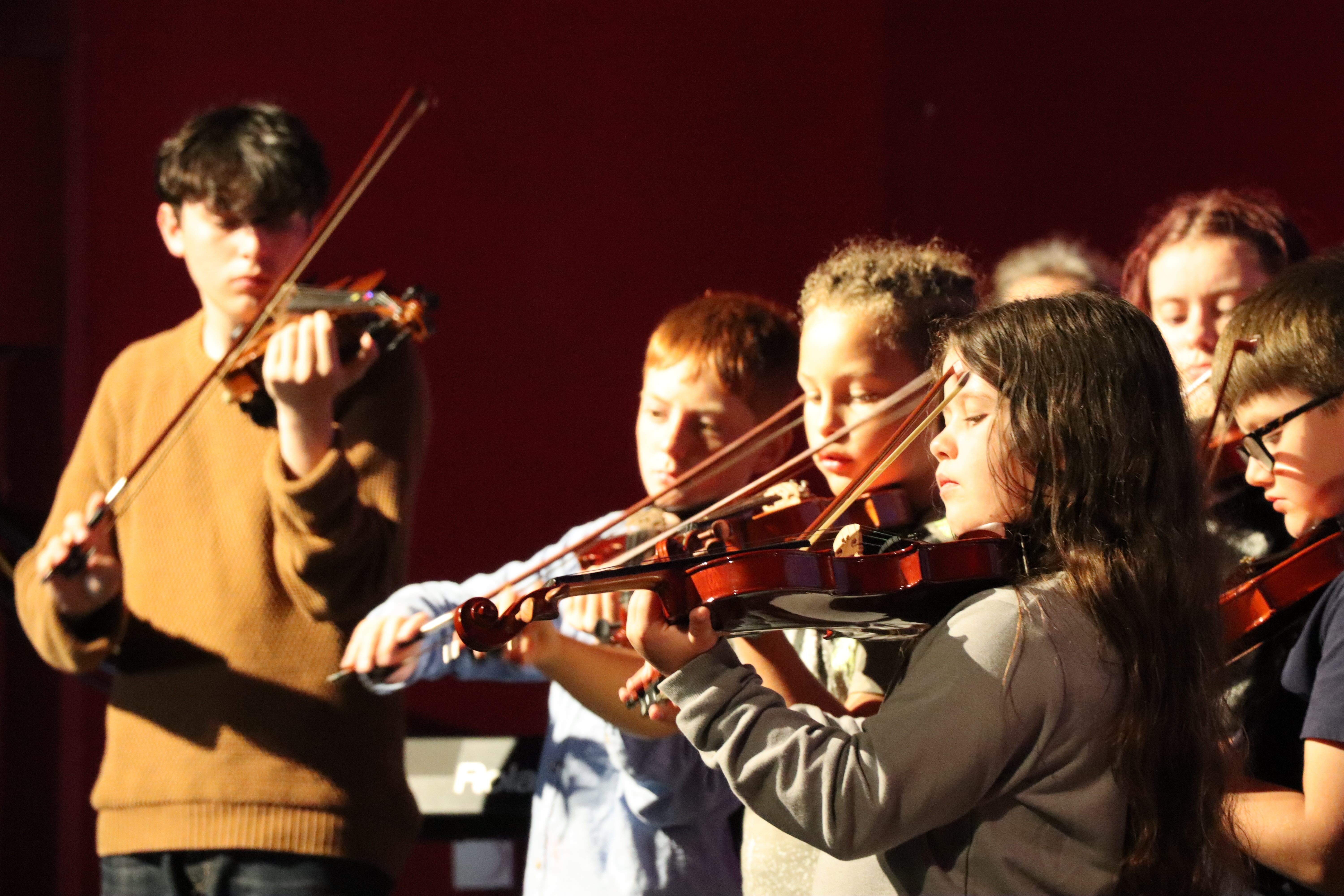 A group of young people playing violins on stage at the Palace Court Theatre, Bournemouth.