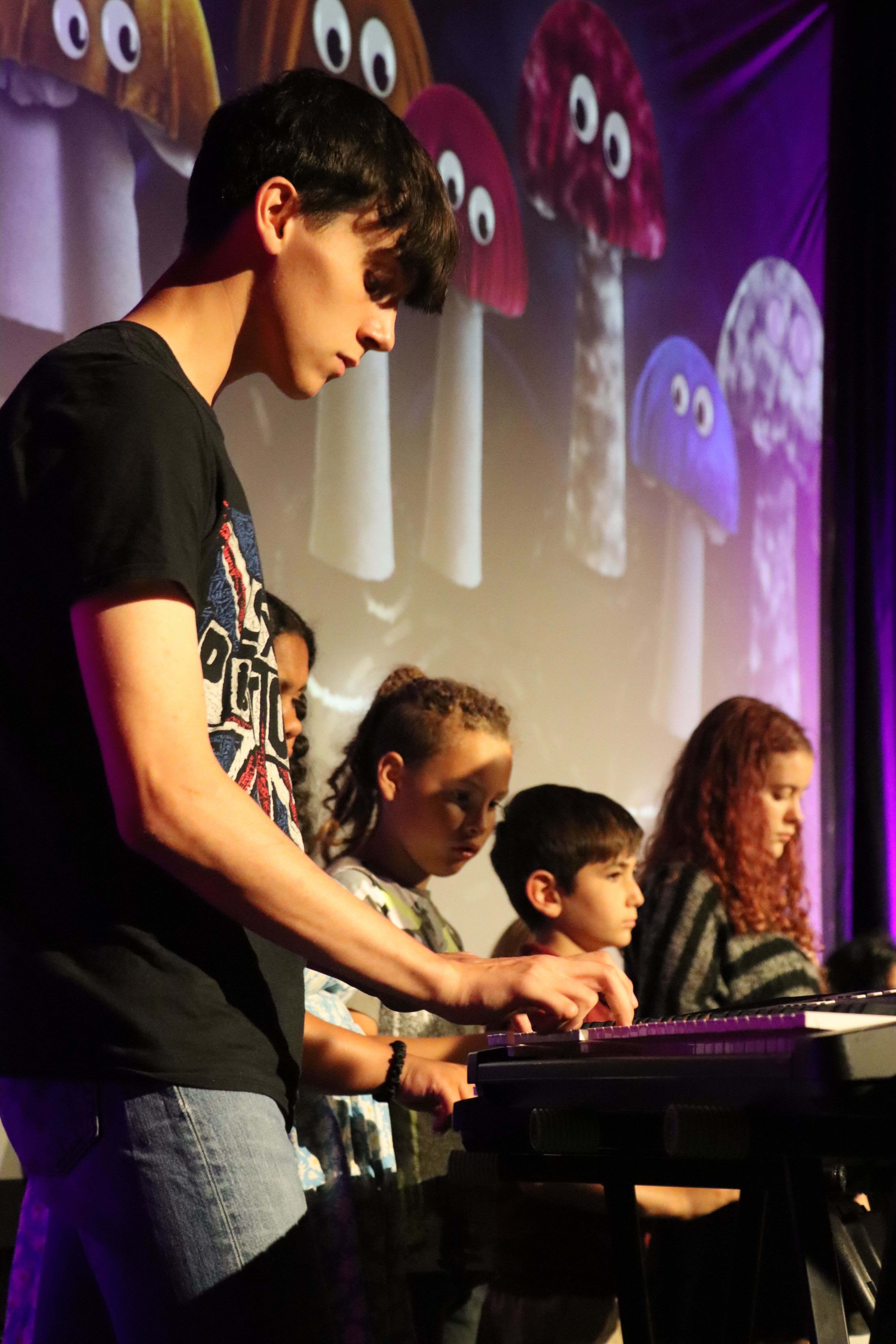 A young person playing an electric keyboard, with other young musicians in the background, on stage at the Palace Court Theatre, Bournemouth.