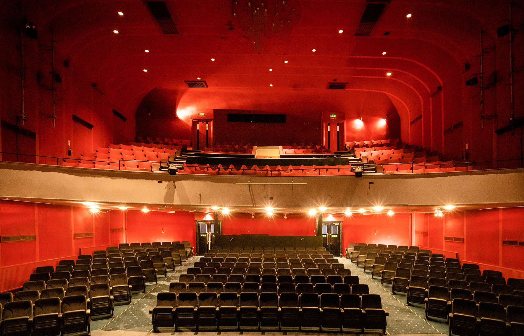 The inside of a theatre auditorium, with three columns of seats on the ground floor and a balcony with further seating above it.