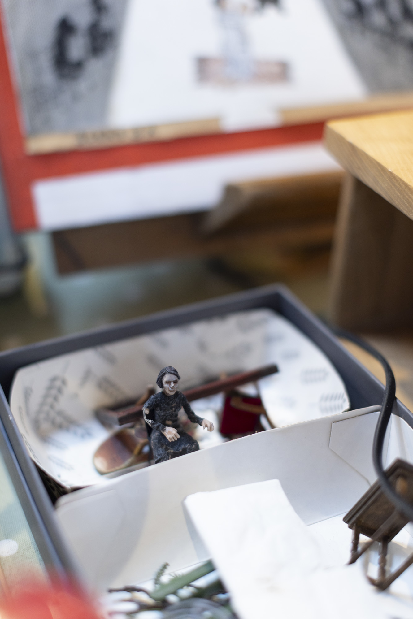 Miniature character next to miniature wooden furnitures in a white box.
