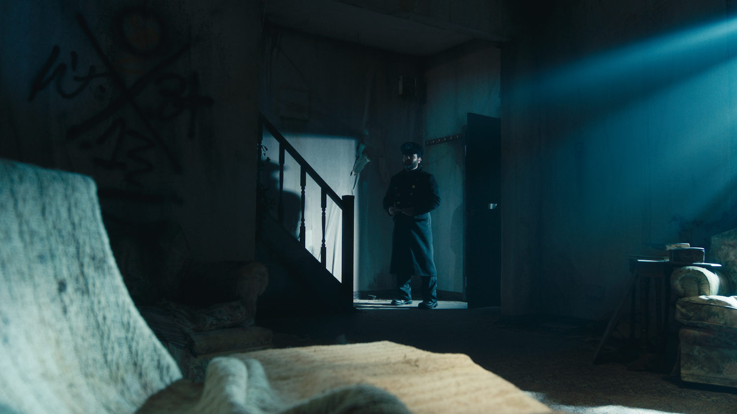 Dark interior with figure silhouetted in doorway, blue light streaming through windows, curved white surface in foreground.