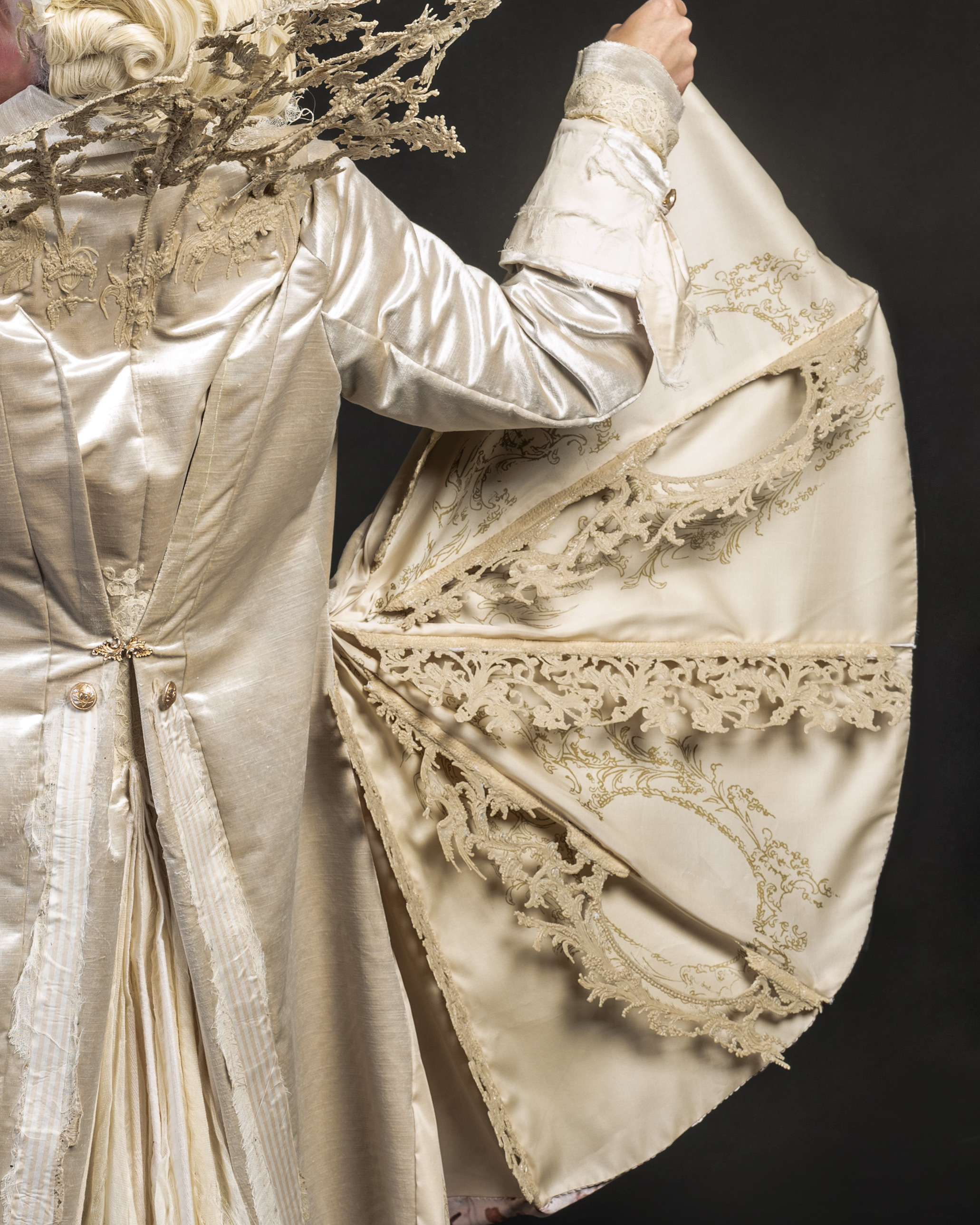 Ivory silk historical dress with elaborate gold embroidered trim and lace details, full skirt with ornate decorative bands displayed on mannequin.
