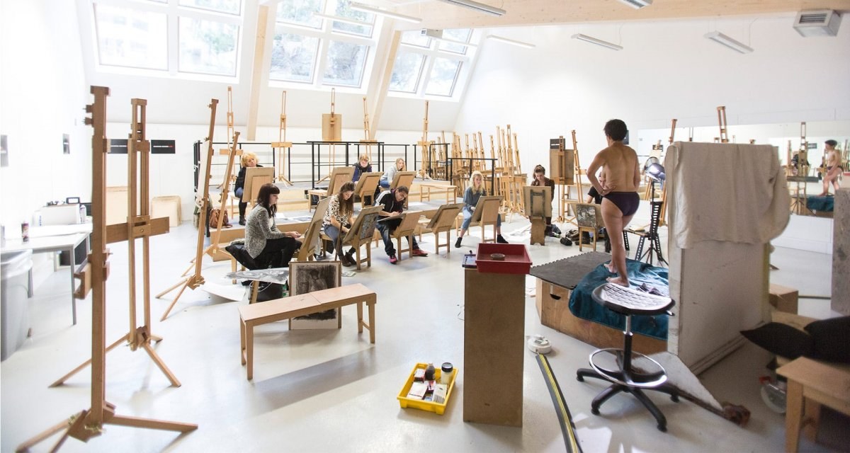 Two rows of artists working on easels while a model poses for them on a platform.