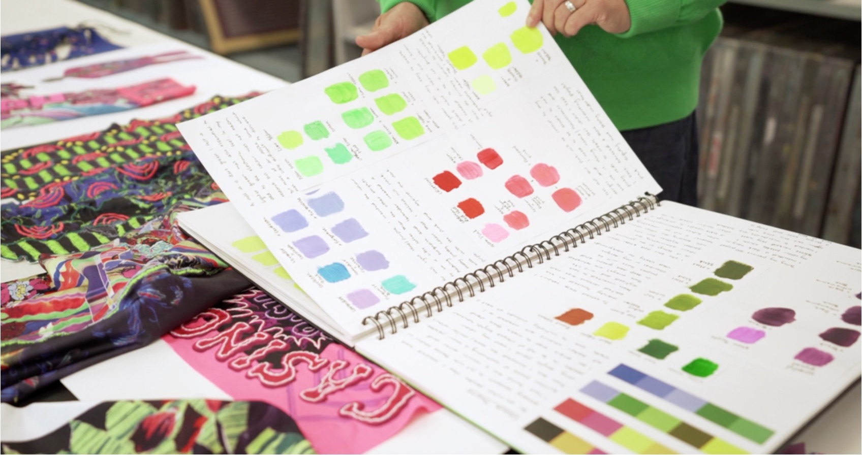 A list of colour swatches on a table with textile work.