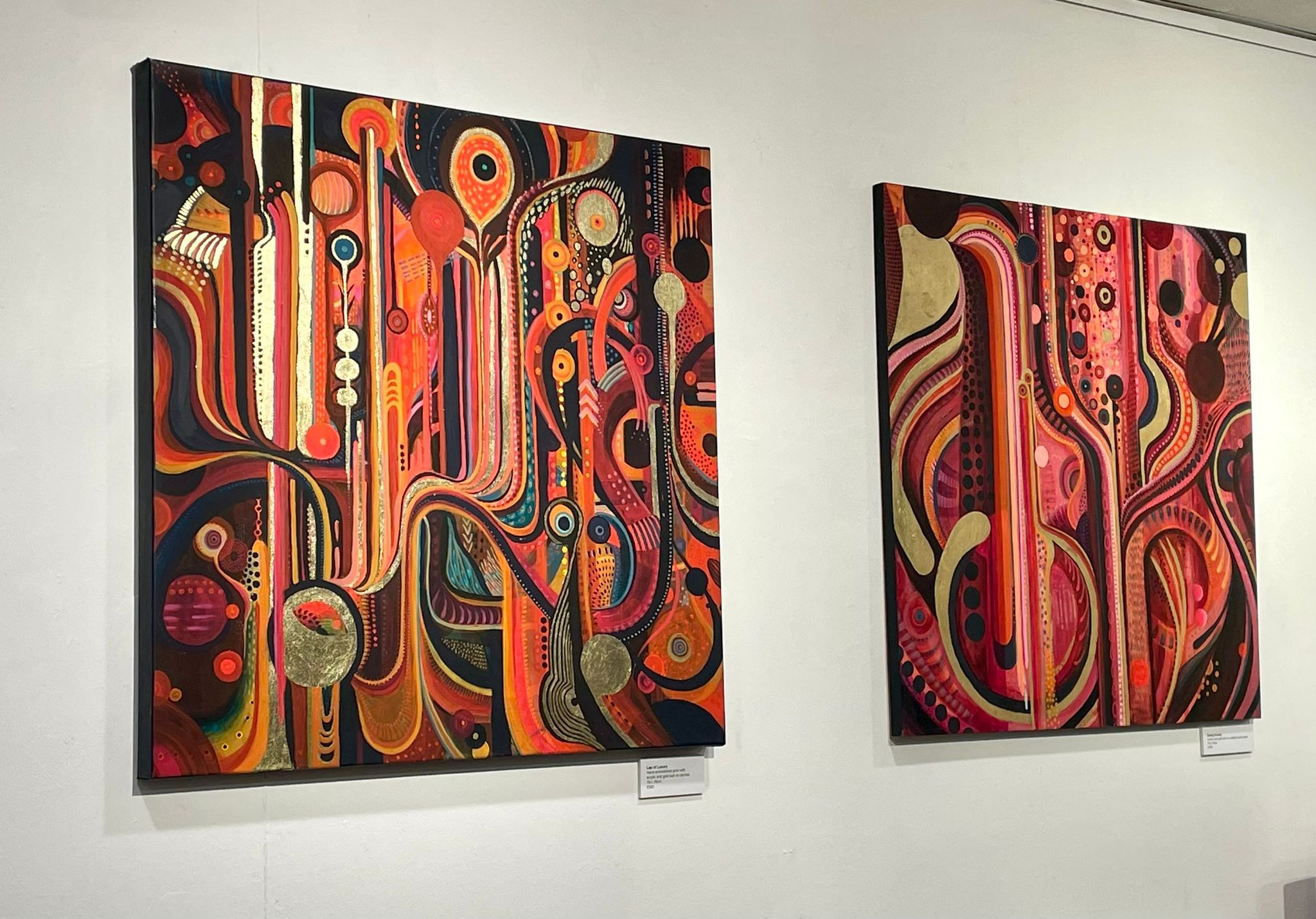 Two abstract paintings on white wall featuring flowing curved lines and geometric shapes in warm tones of red, orange, and brown.