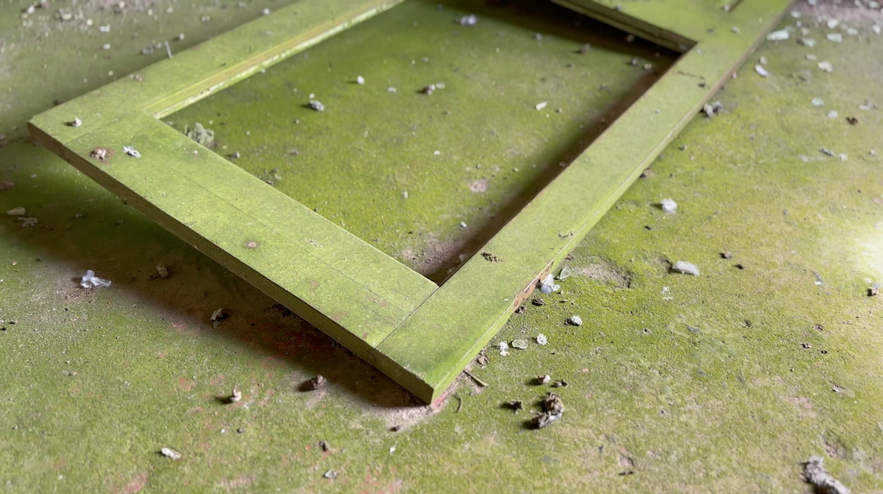 Green wooden frame partially submerged in muddy water with debris and leaves scattered around on wet ground.