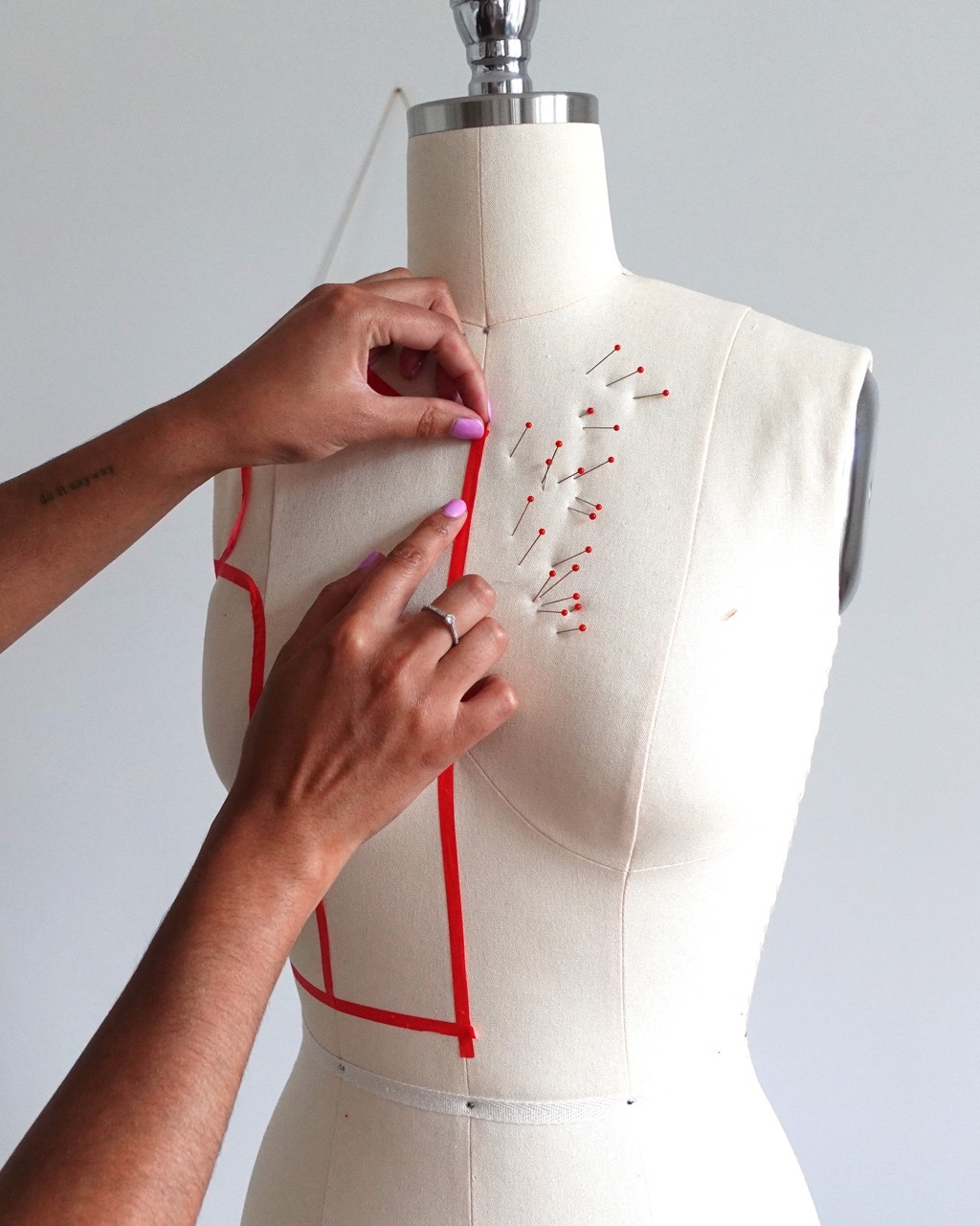 A person holding red tape on a fabric mannequin with red pin sticks out the side.