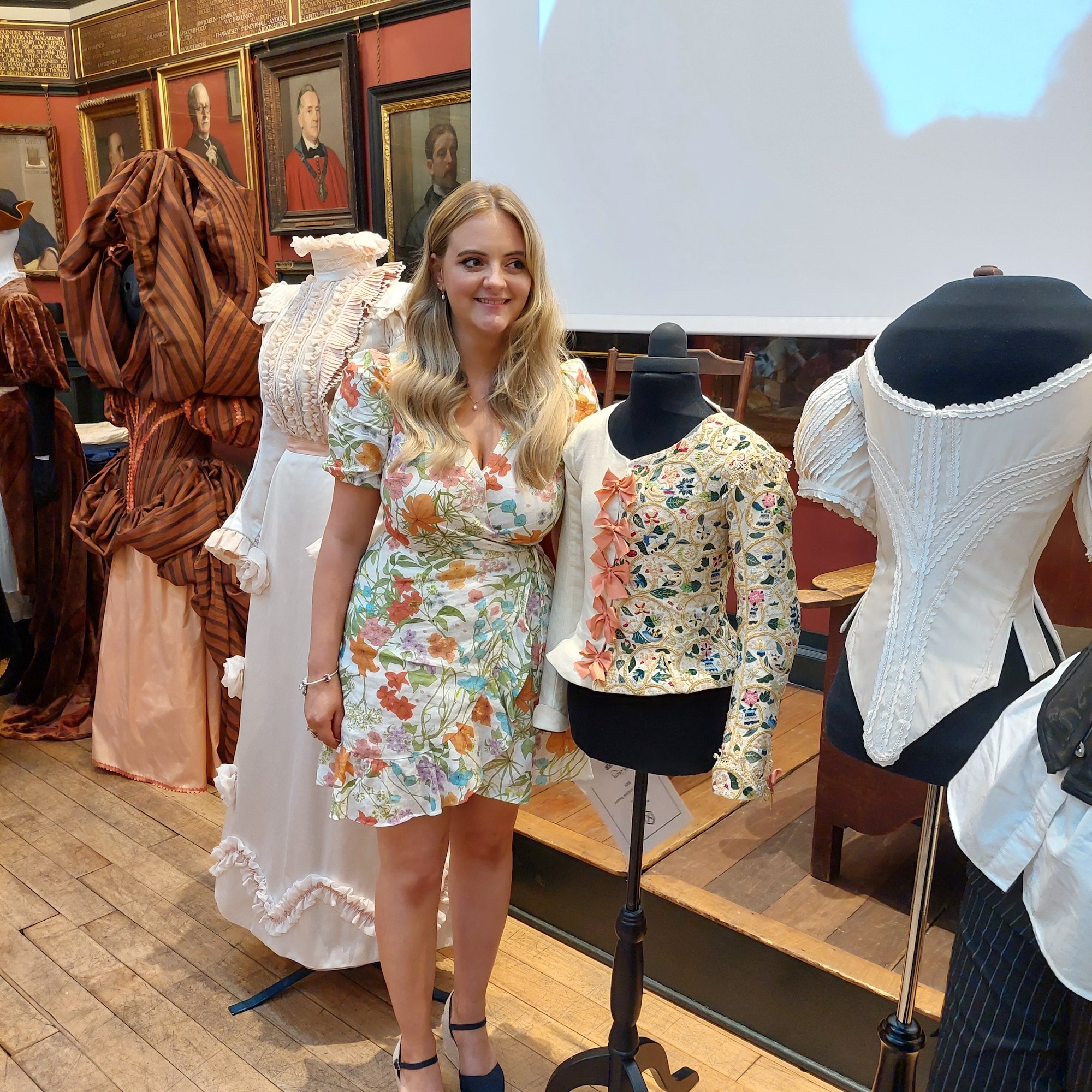 BA (Hons) Costume graduate Beth Lacey poses for a photo next to her embroidered jacket, displayed on a mannequin, at the Patterns of Fashion Awards 2023.