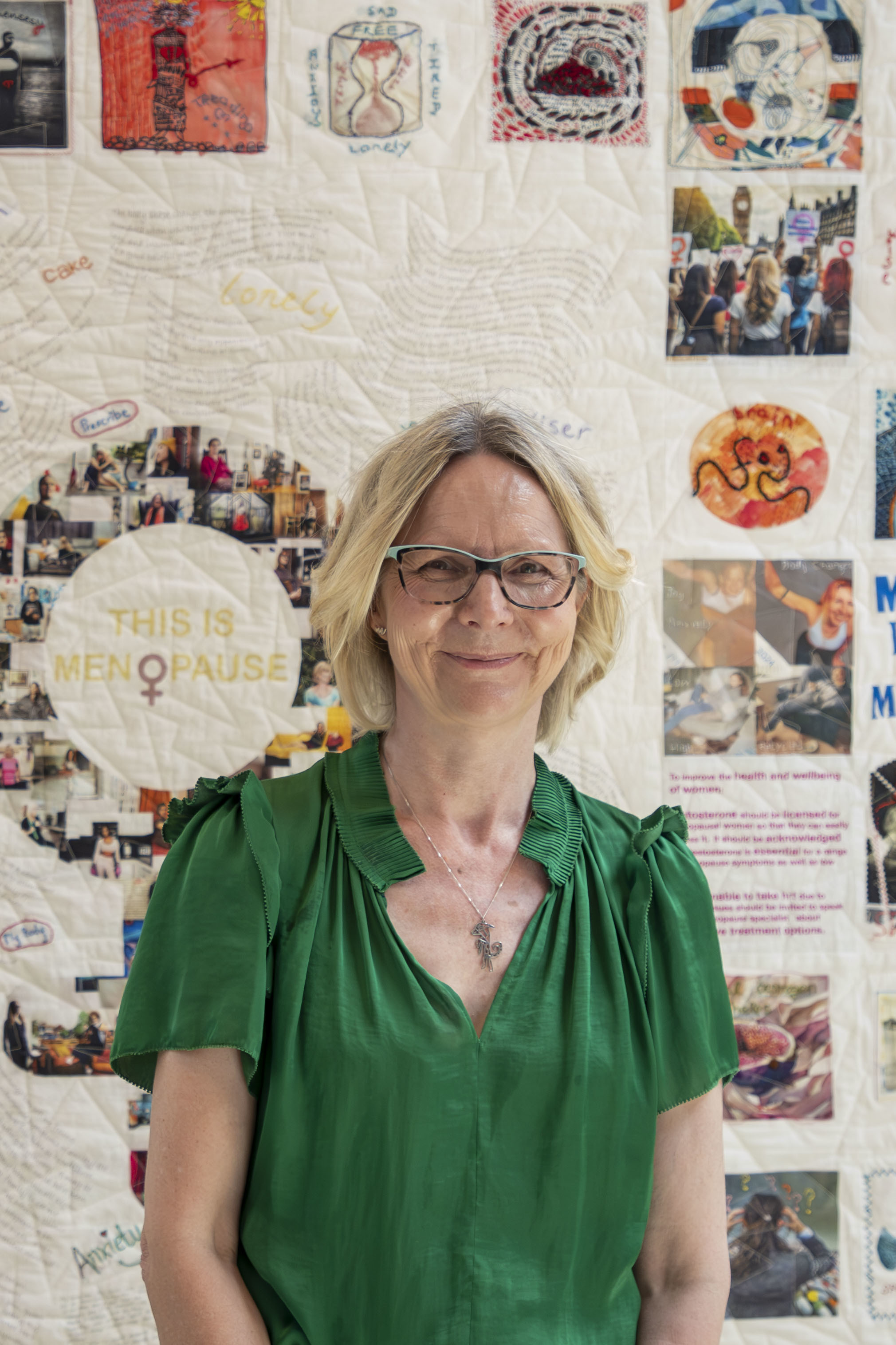 Portrait of P Ferrick-Squibb standing in front of the menopause quilt.