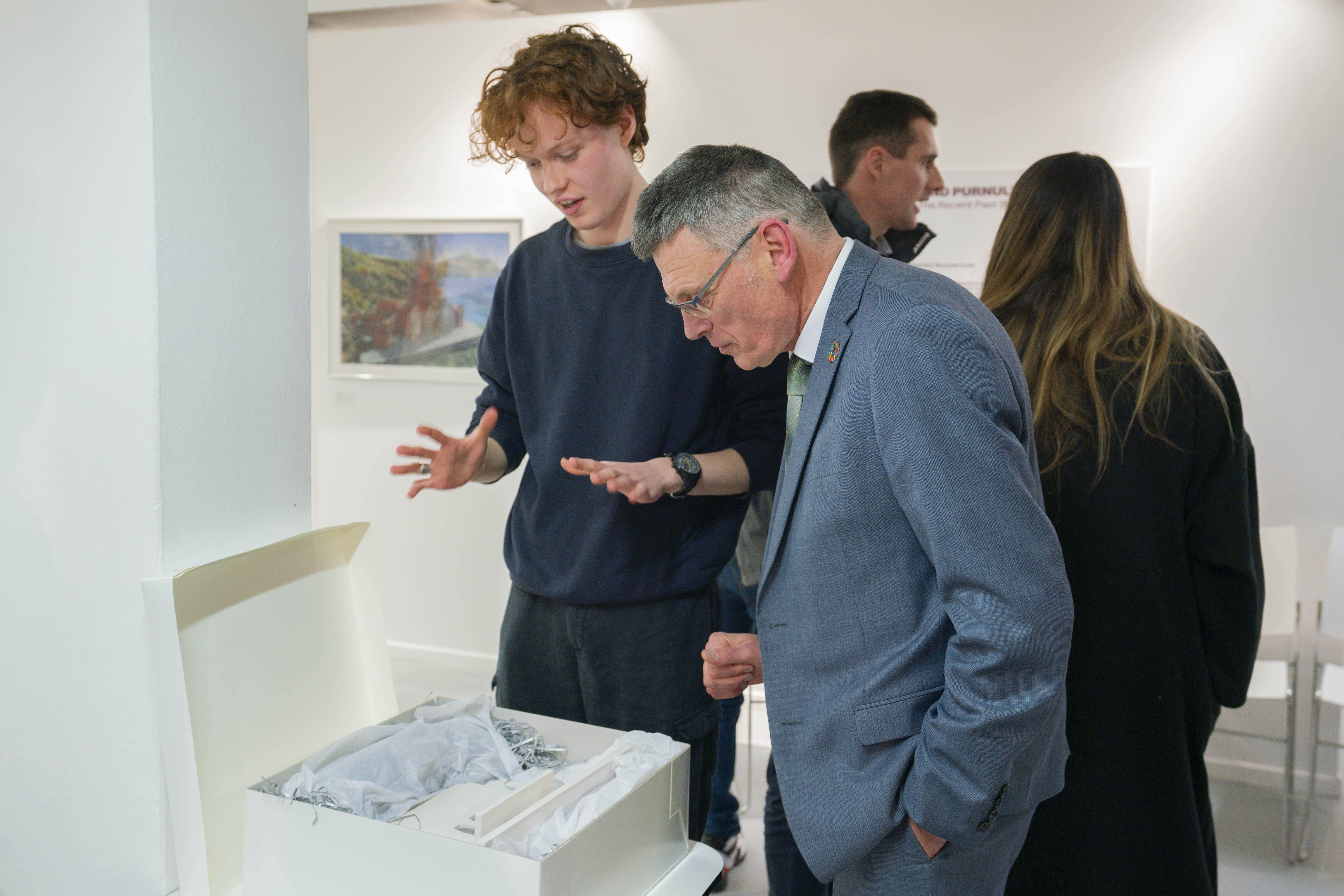 Professor P Gough speaking with an alumnus and looking at a model in a box at an exhibition at TheGallery, AUB.