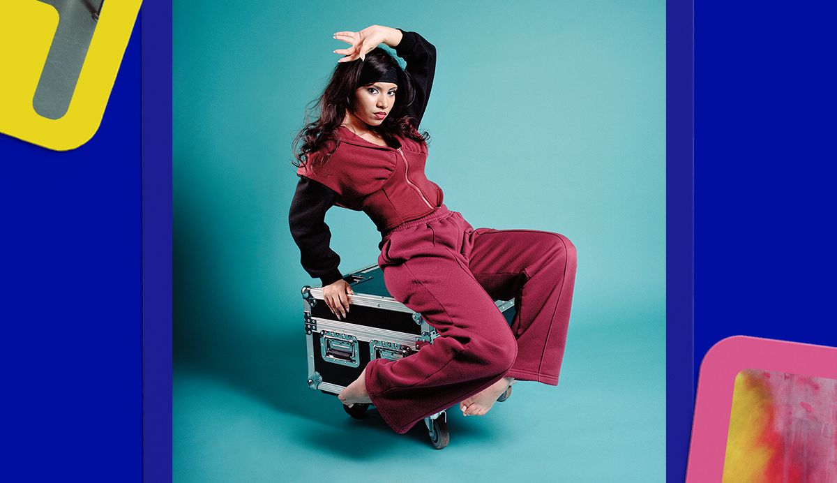 Woman in red tracksuit sitting on metal suitcase against turquoise background, framed by blue and yellow geometric shapes.
