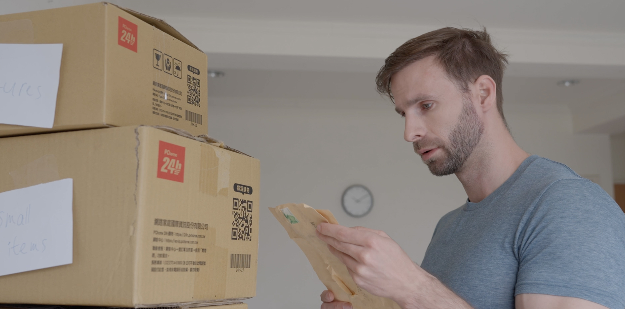P Kertesz in "Found and Forgiven" reading delivery label on stacked cardboard boxes indoors.