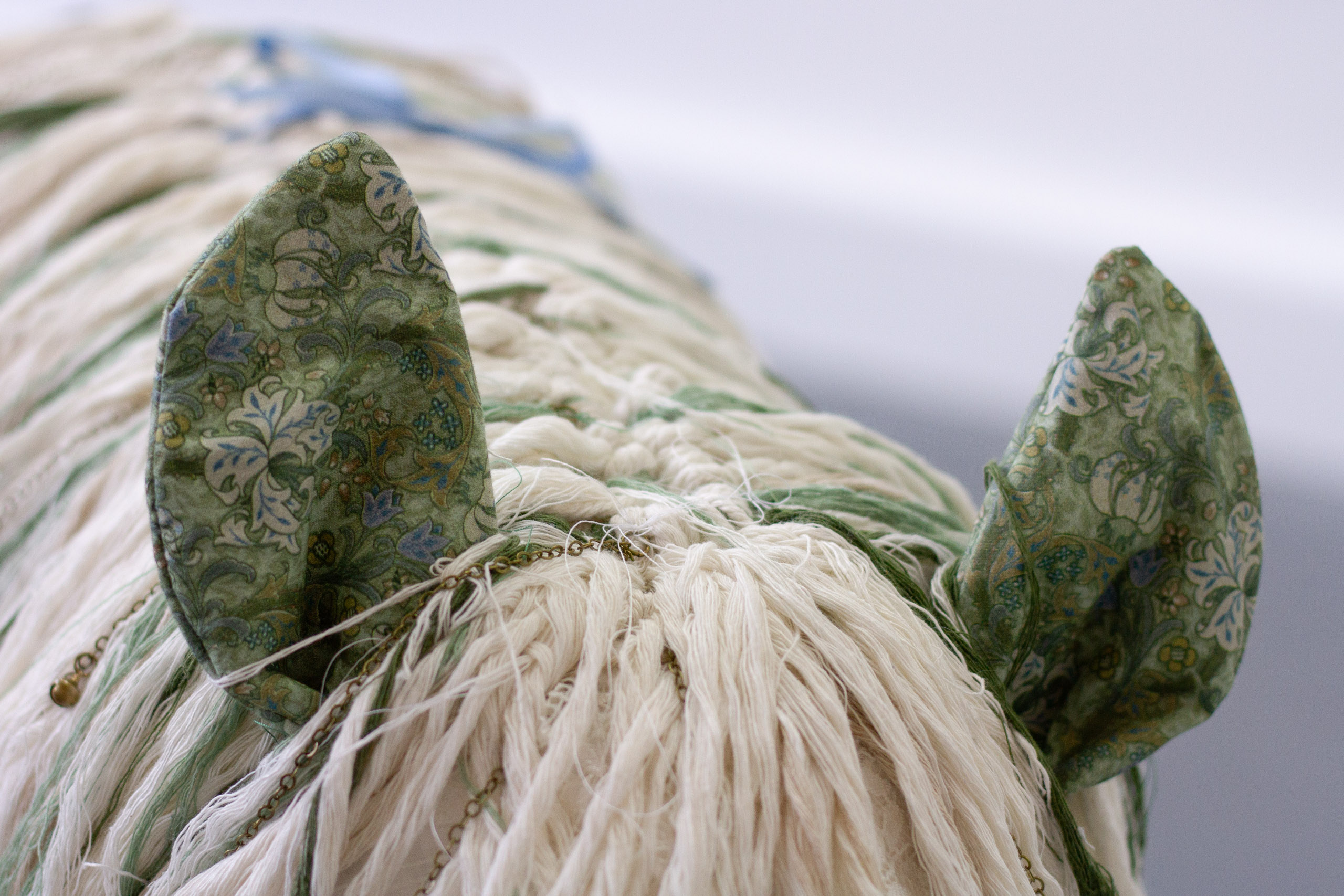 Close-up of a horse sculpture's ears, made from green, patterned soft materials.